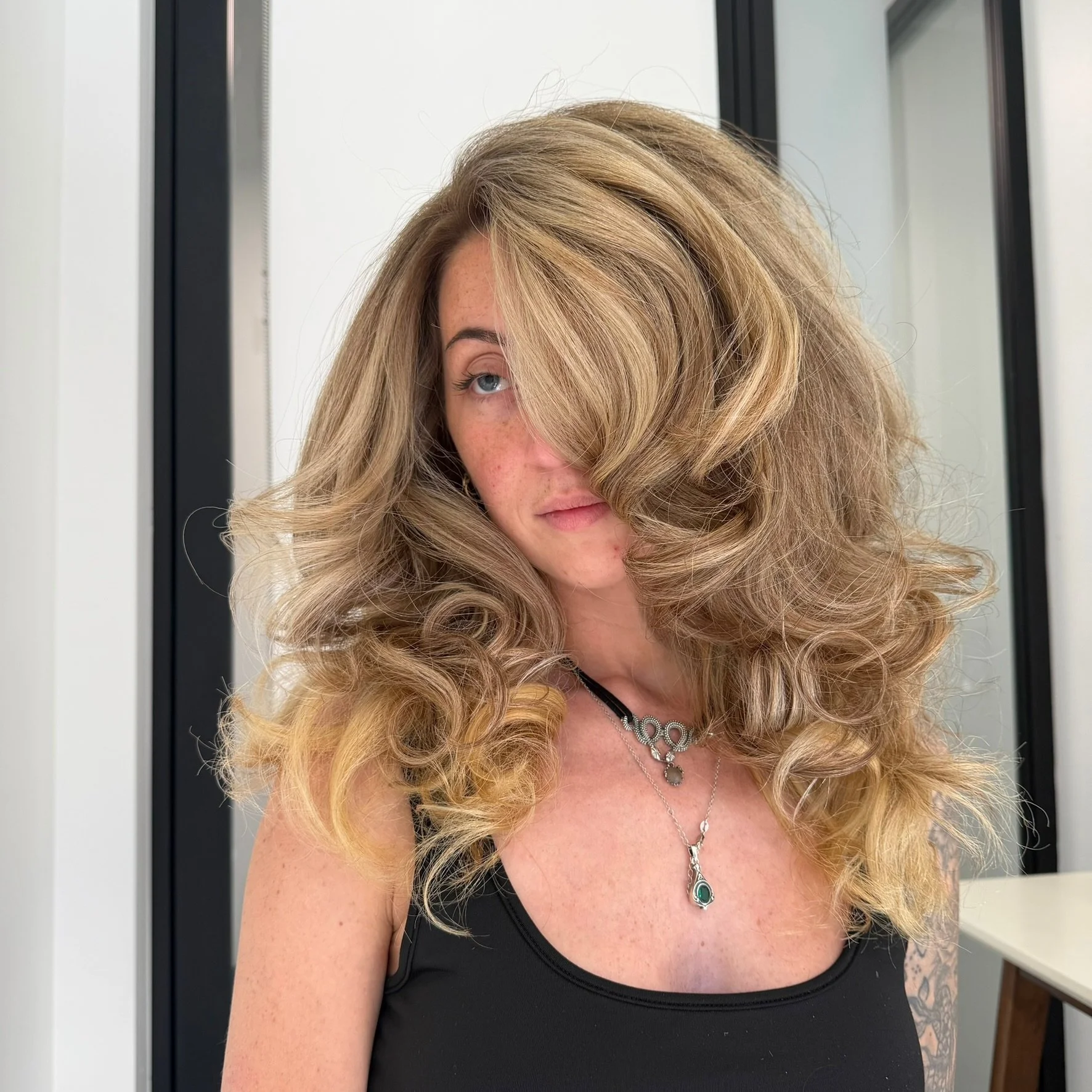 A female client in a black tank top with a fresh hair cut, voluminous blow out and fresh highlights.