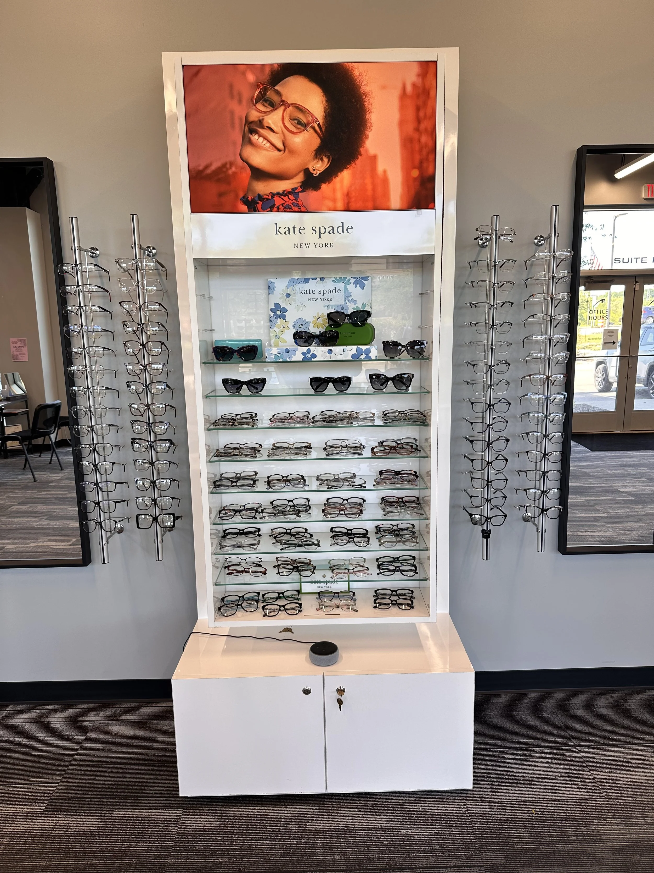 Display of eyeglasses and sunglasses at a Kate Spade store, with a large advertisement featuring a smiling woman wearing glasses at the top.