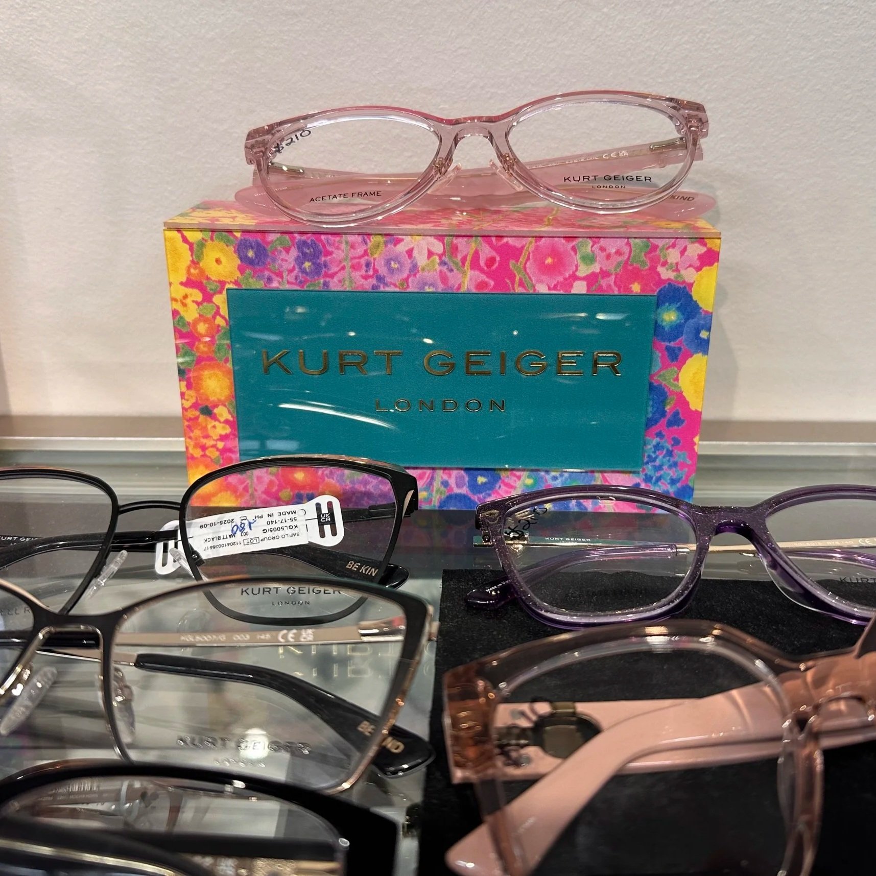 Display of various sunglasses on a black surface with a colorful box labeled 'Kurt Geiger London' in the background.