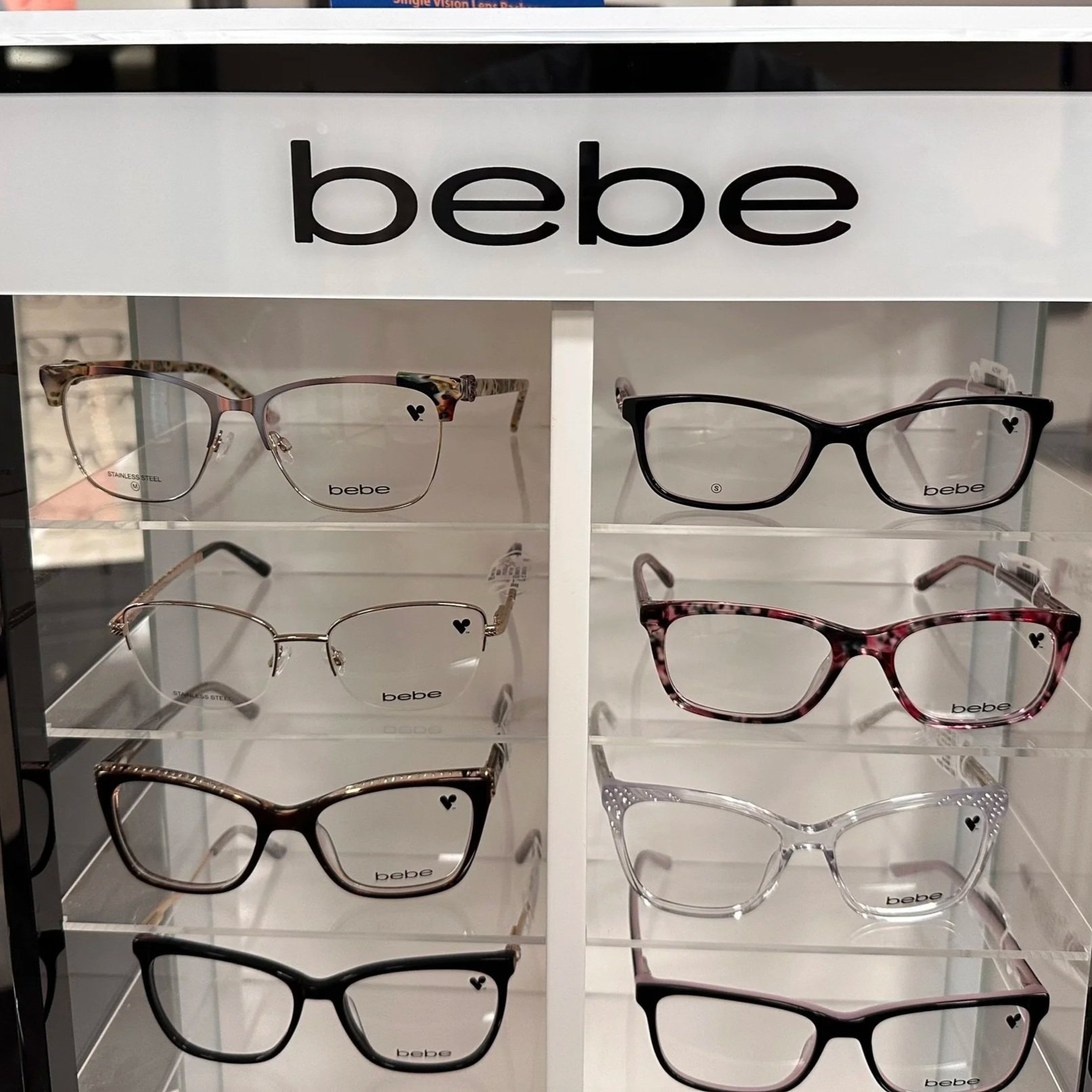 Display of eyeglasses on shelves at a store, with a white sign labeled 'bebe' above.