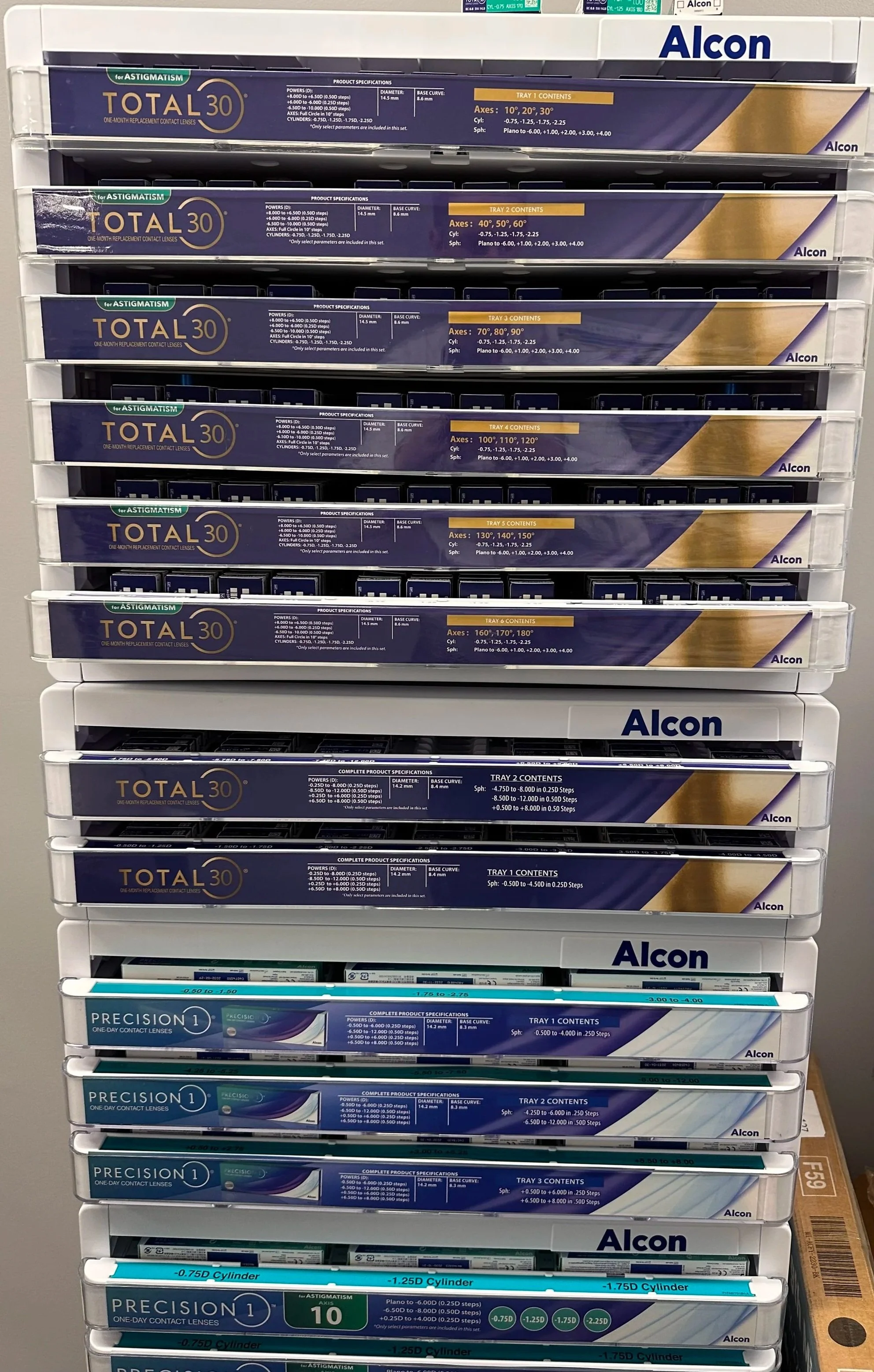 Display of multiple boxes of contact lenses arranged on a rack, with branding such as 'Total 30' and 'Precision 1'.