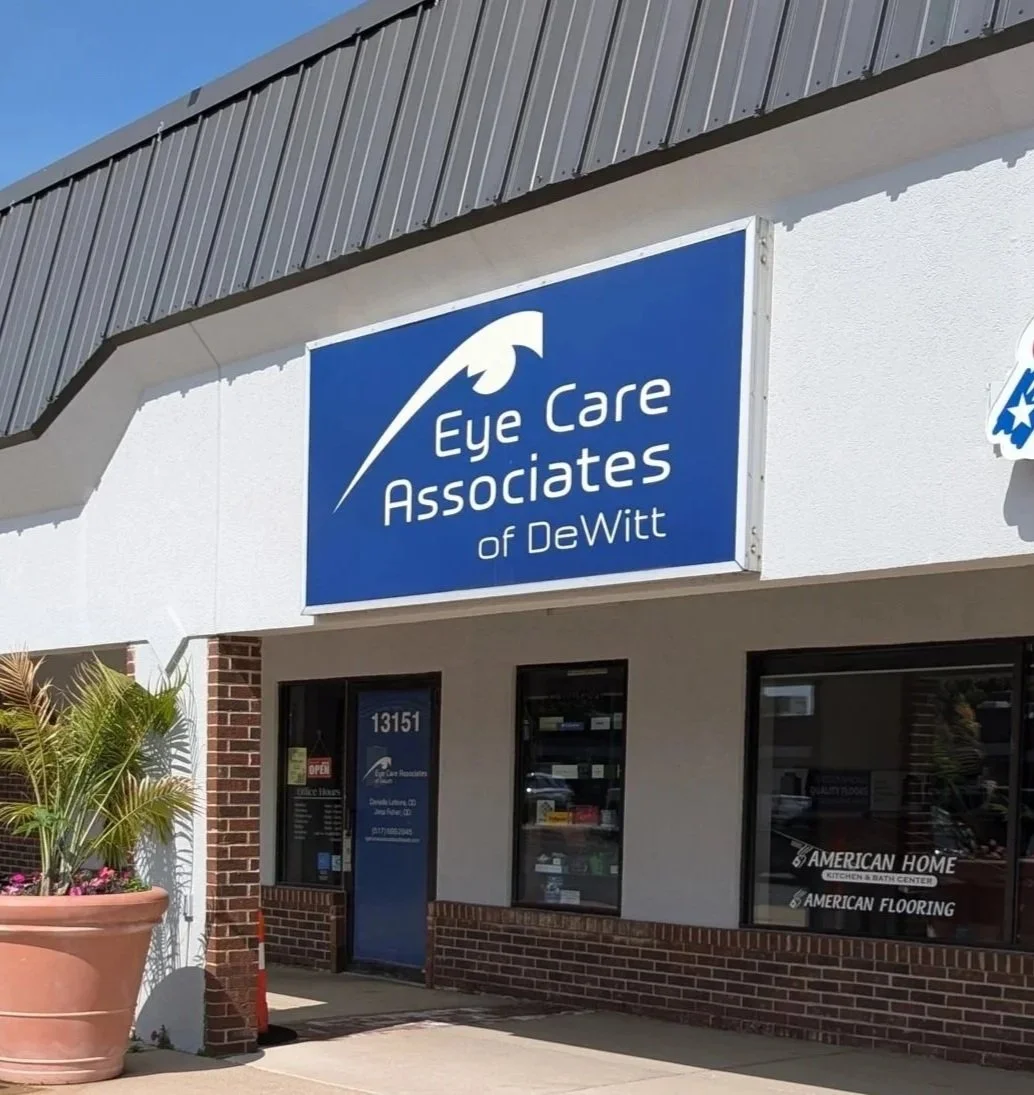  storefront with a blue sign that reads 'Eye Care Associates of DeWitt' along with an eye logo. There is a potted plant outside and windows displaying additional business information.