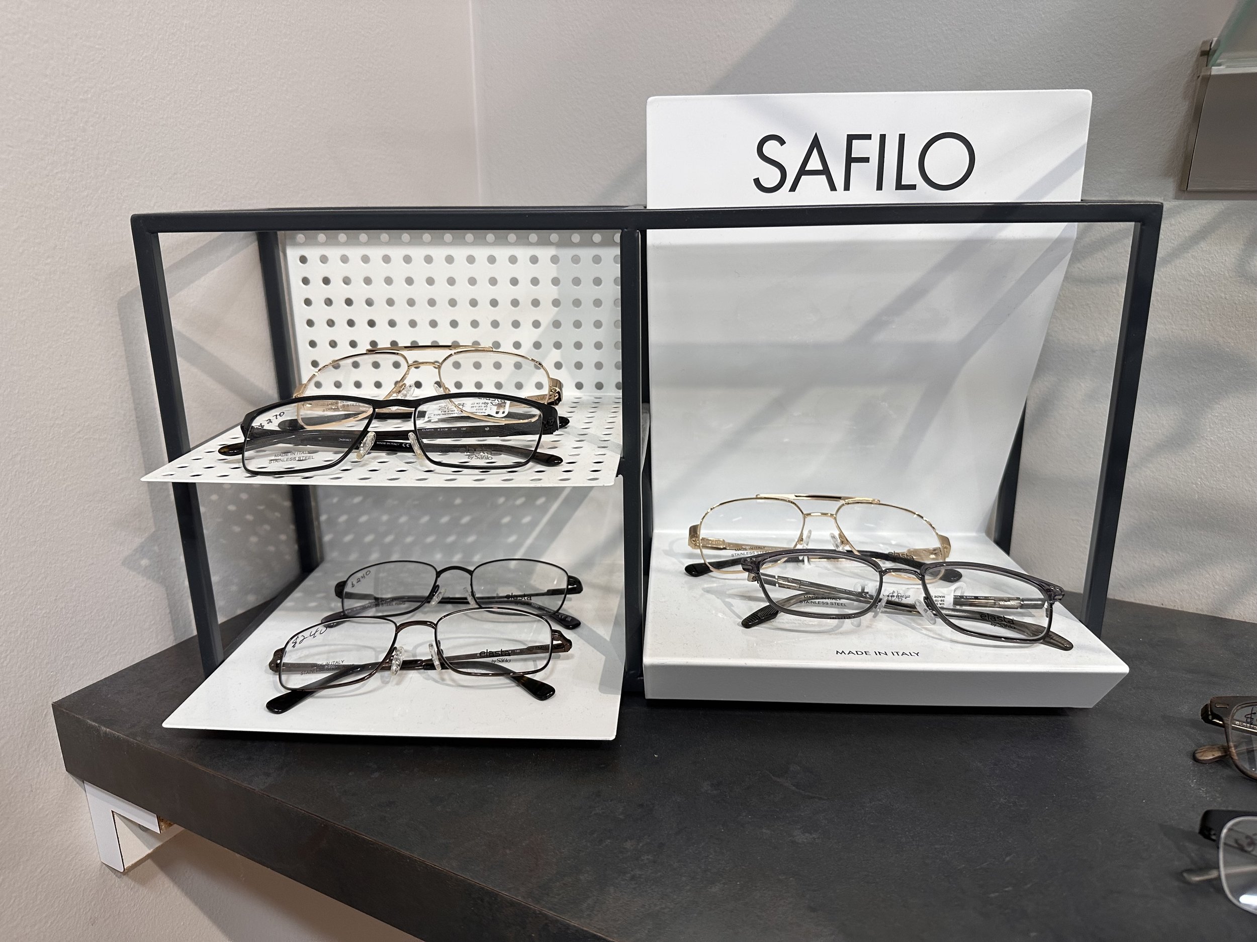 Display of eyeglasses on a white shelf with a black frame, with a sign reading 'SAFILO' on top and a label 'MADE IN ITALY' at the bottom right.