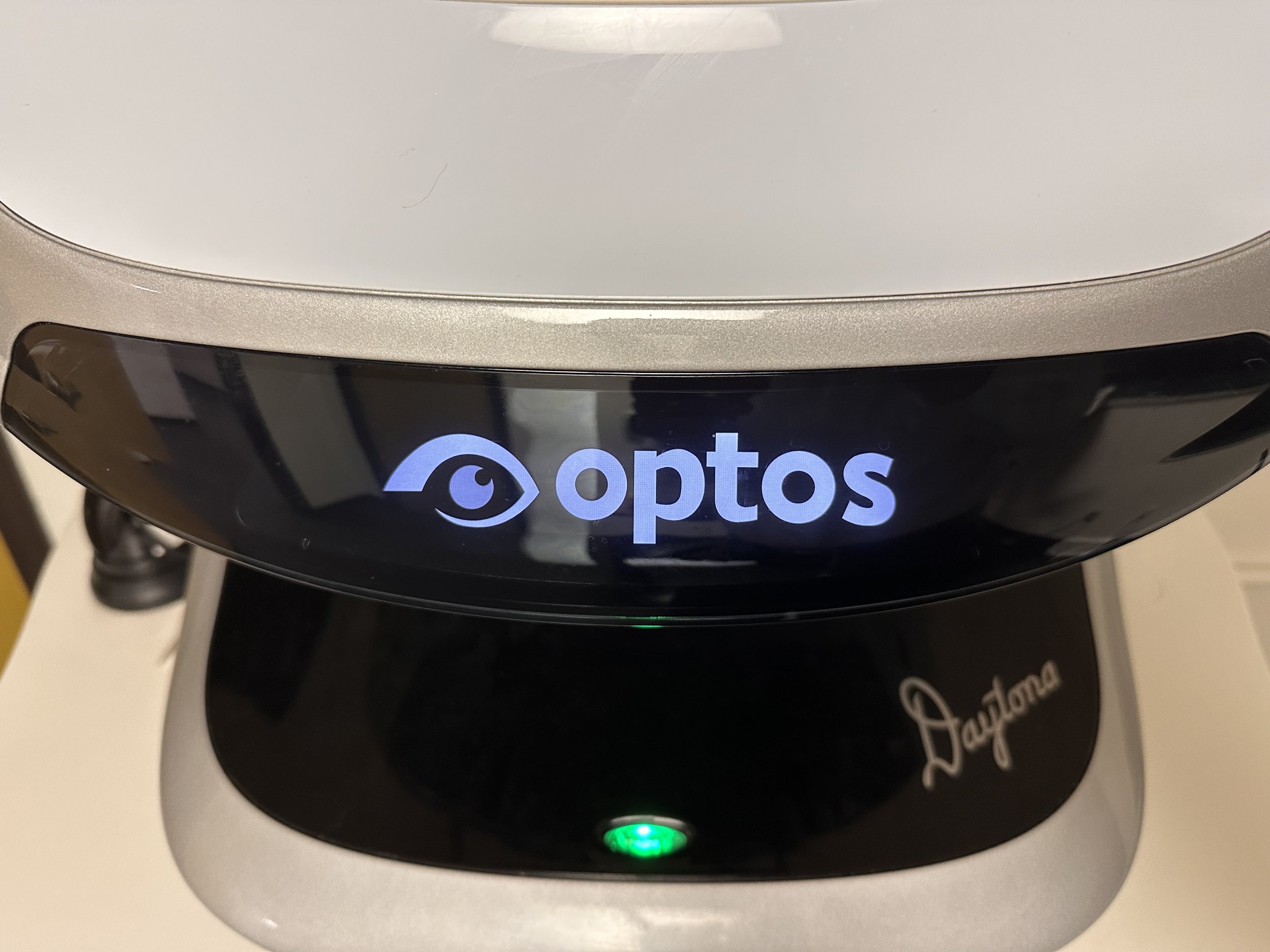 Close-up of a black coffee machine with a digital display showing the word 'optis' and a green indicator light, placed on a white surface.