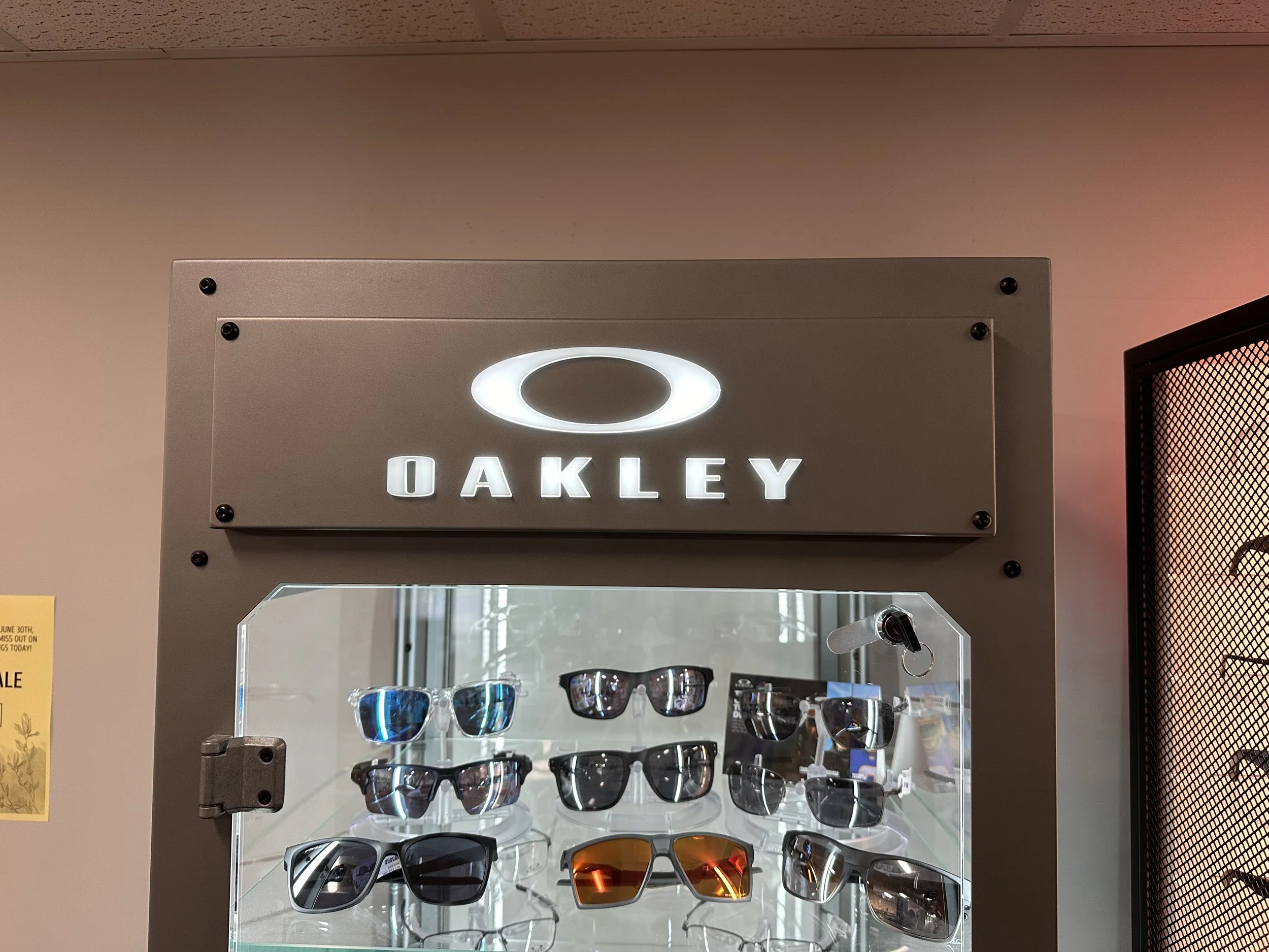 Display case with Oakley sunglasses, illuminated with a sign above reading 'OAKLEY' in white letters with a circular logo.