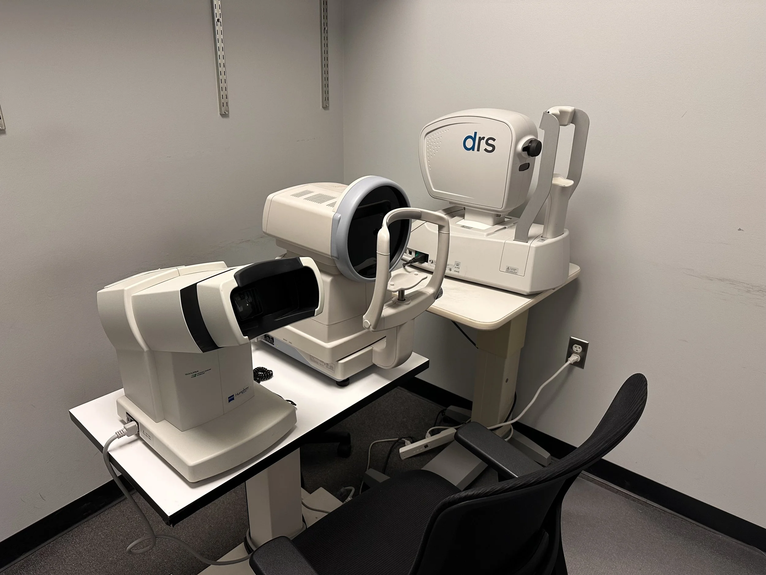 Medical imaging equipment, specifically an ophthalmic device, placed on a table in an examination room with a chair nearby.