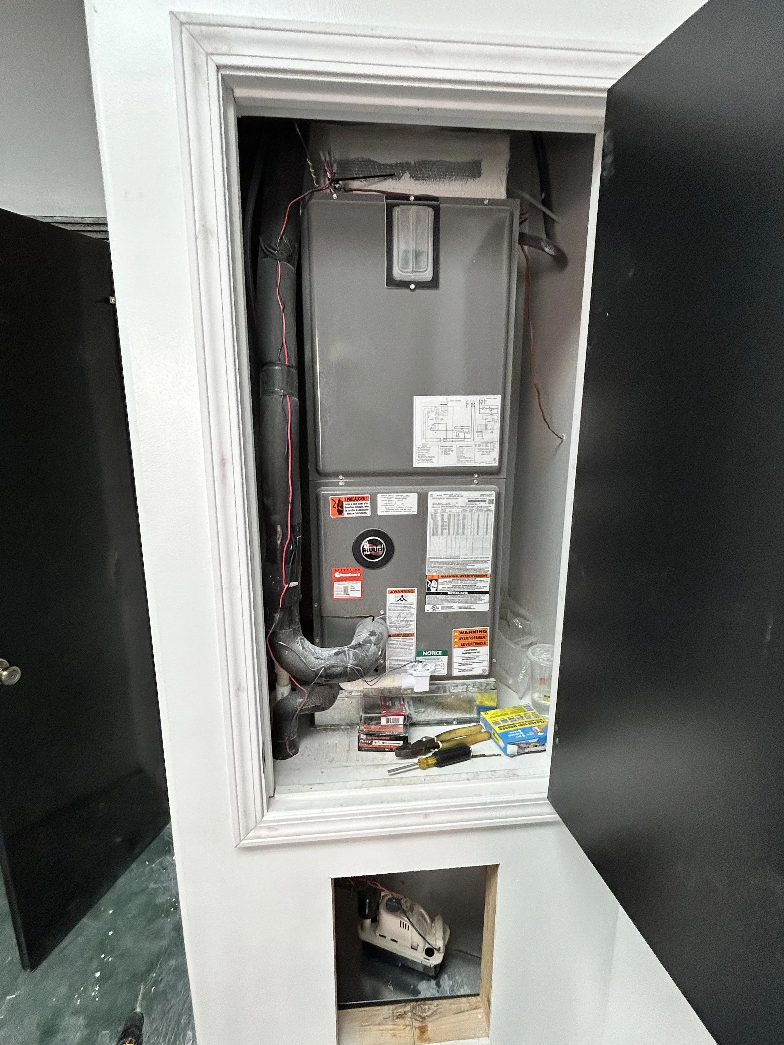Inside a laundry room or utility closet with an HVAC furnace or air handler, tools like screwdrivers and a level, and some packages or cleaning supplies at the bottom.