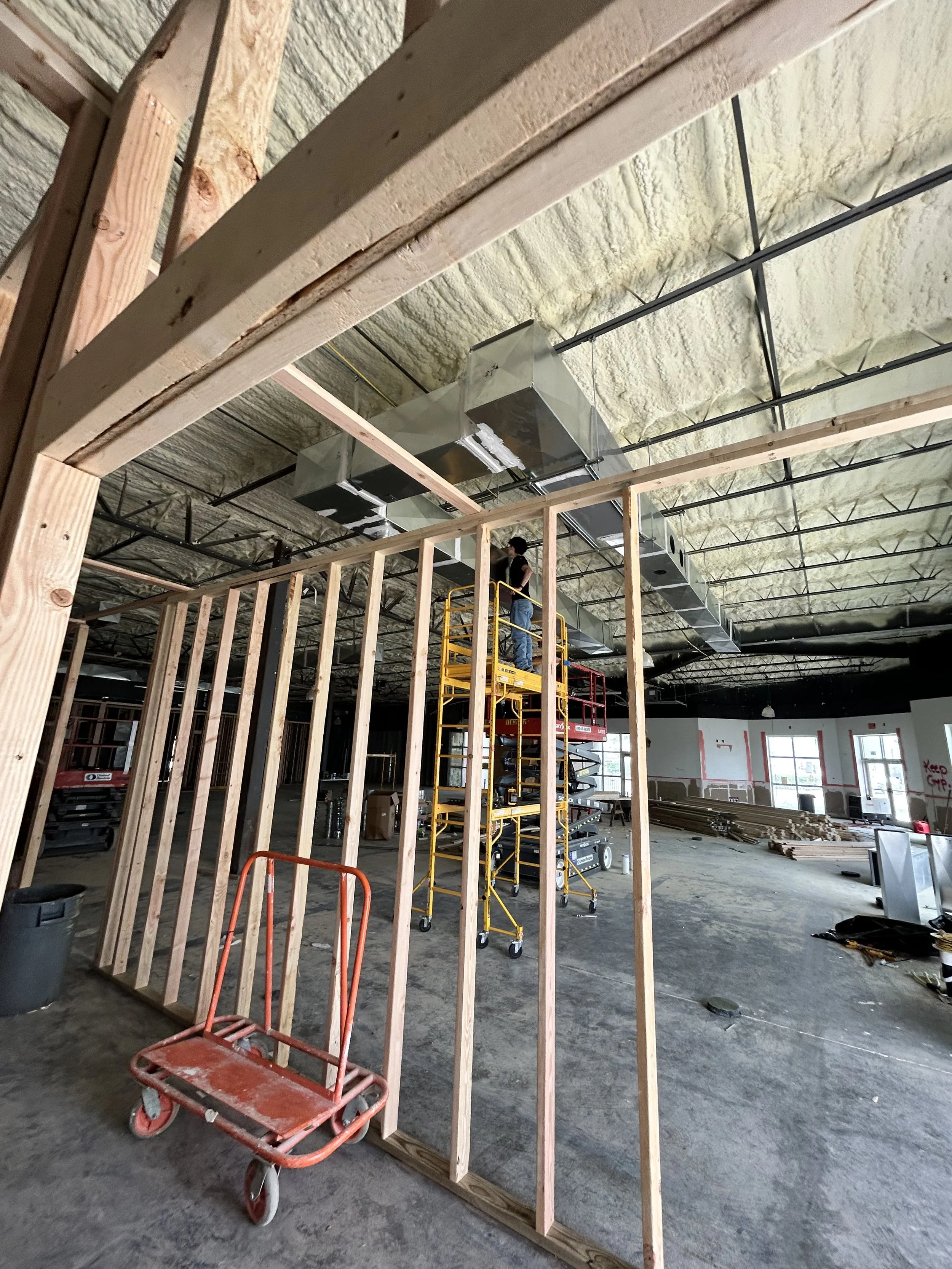 Construction site with exposed wooden framing, scaffolding, and ductwork in progress inside a building.