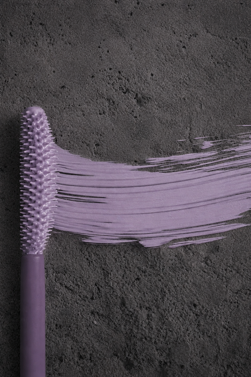 A purple brush with long, flexible bristles laying on dark, textured sand.