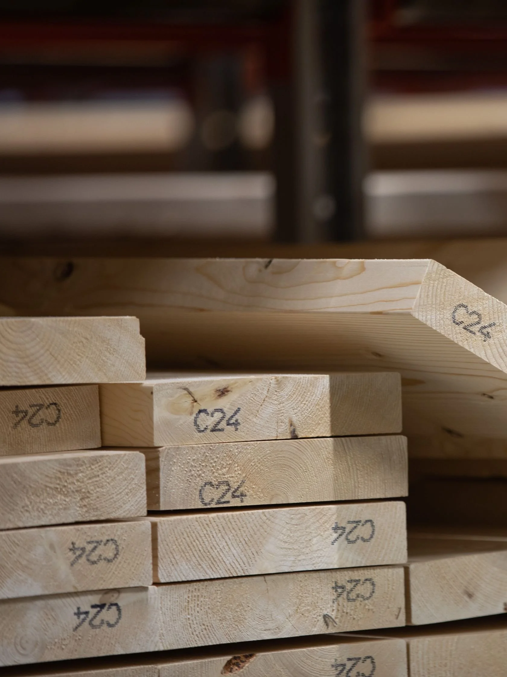 Stacked wooden planks with markings, mostly light-colored pine wood, in a construction or woodworking setting.
