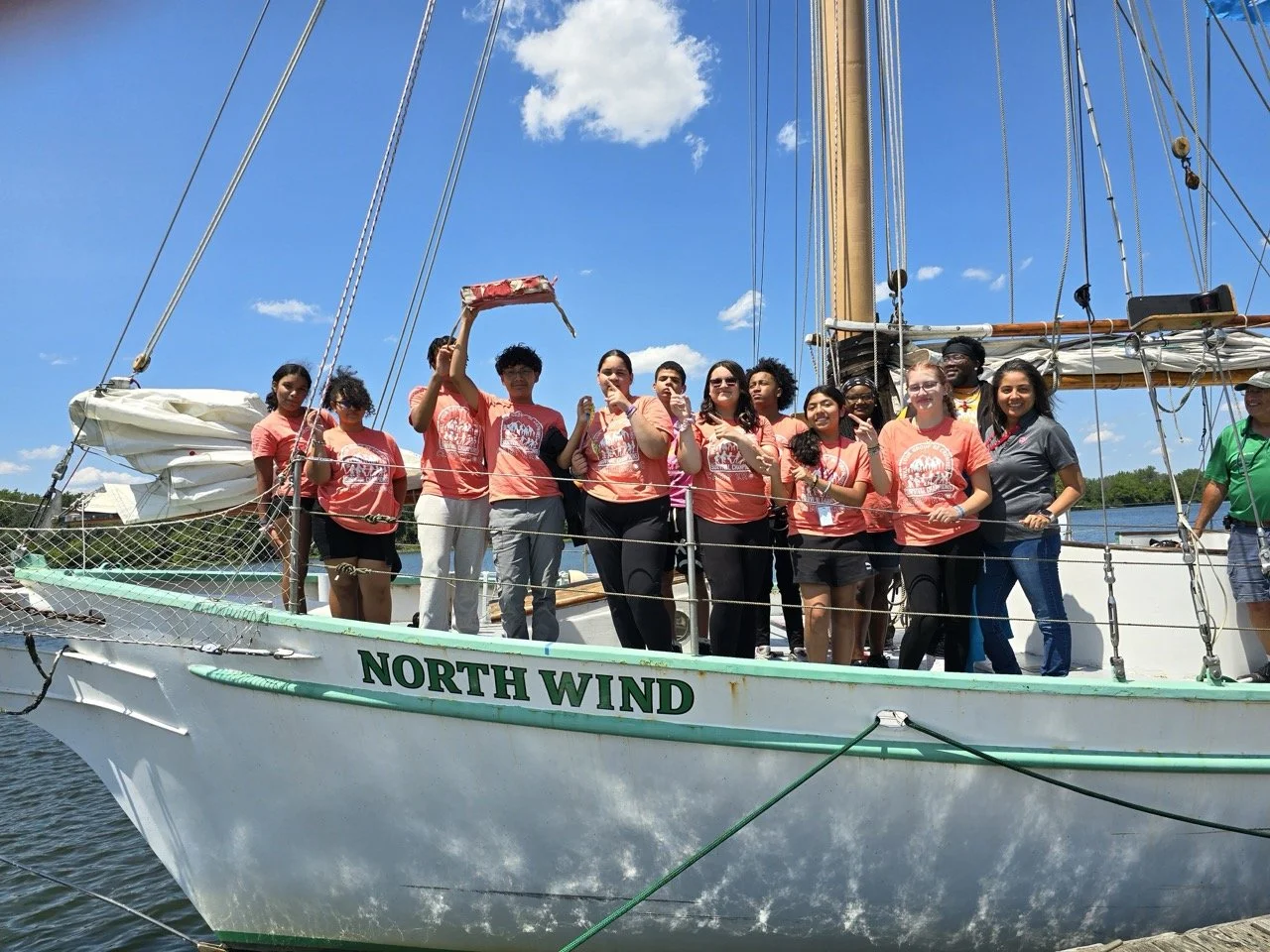 A group of people standing on a boat named North Wind, celebrating outdoors on a sunny day with blue skies and some clouds.