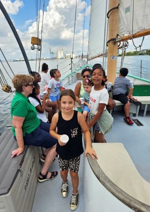 Children and adults on a boat enjoying a day on the water, with some holding drinks and looking around.