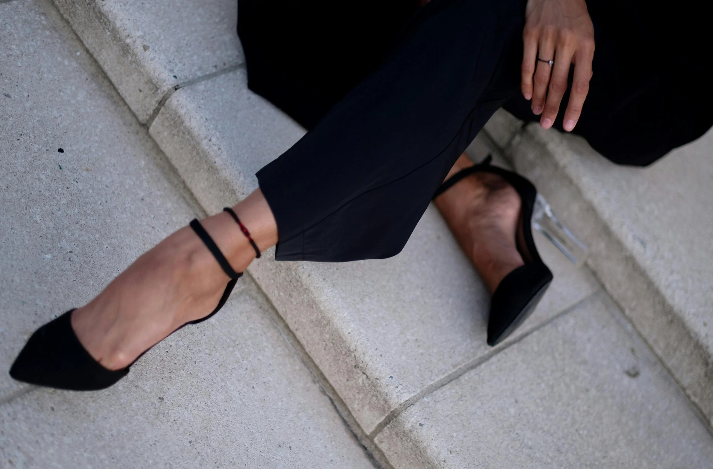 feminine photography showing just the legs of a woman sitting on steps. She is wearing black trousers and black heels with ankle strap.