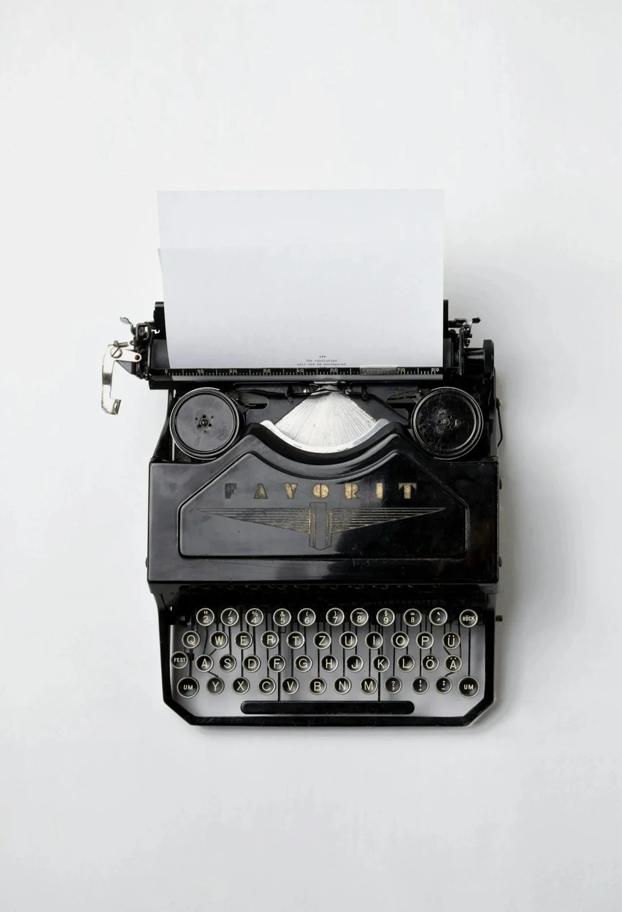 A vintage black typewriter with round keys and a sheet of white paper inserted, placed on a plain white surface.
