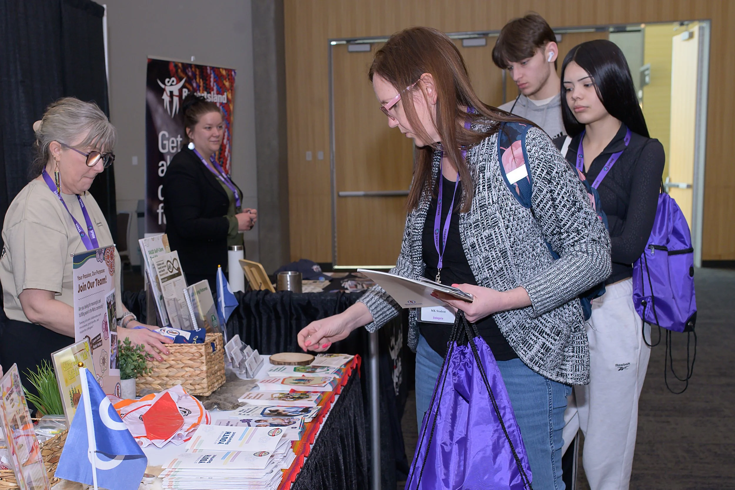 People at an event booth, engaging with informational materials, with brochures and flags on display.