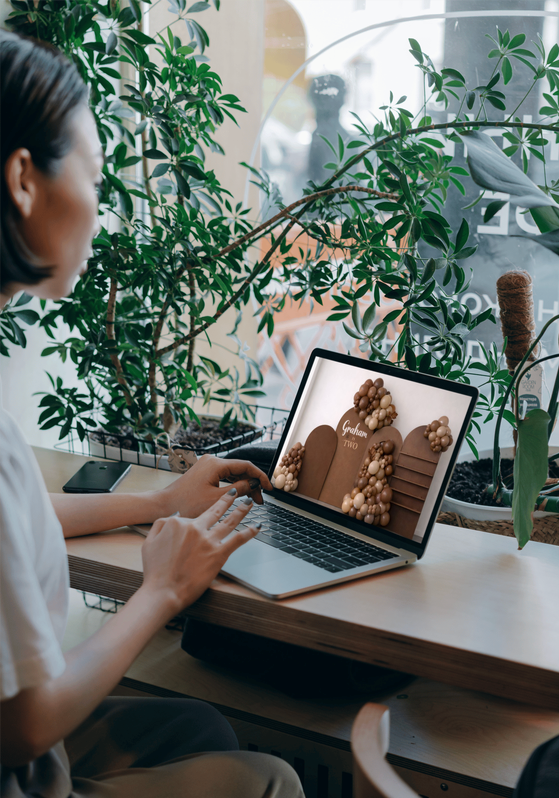 Person working on a laptop at a wooden desk with green houseplants nearby.