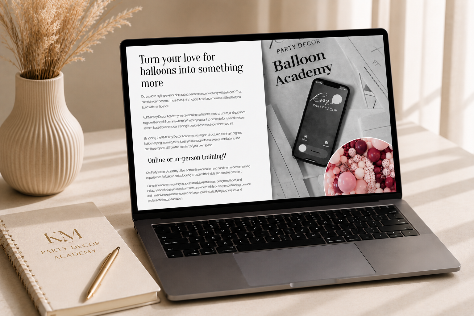 Laptop displaying text and images related to Balloon Academy, a notebook with 'KM PARTY DECOR ACADEMY' on the cover, a gold pen on top, a beige vase with dried flowers, and sunlight streaming through curtains.
