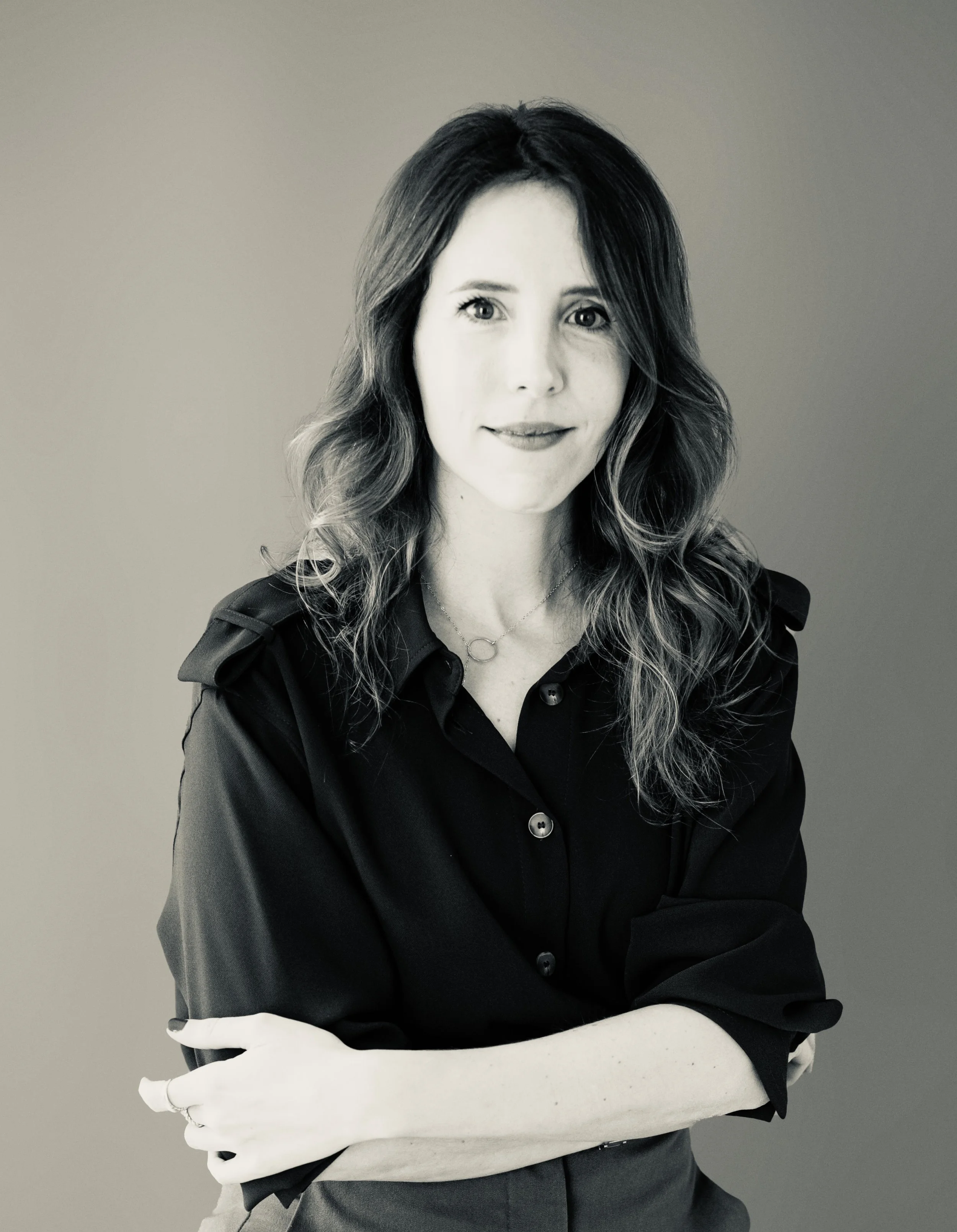 Retrato en blanco y negro de una mujer con cabello ondulado y expresión serena, usando una blusa negra y una cadena con un círculo.