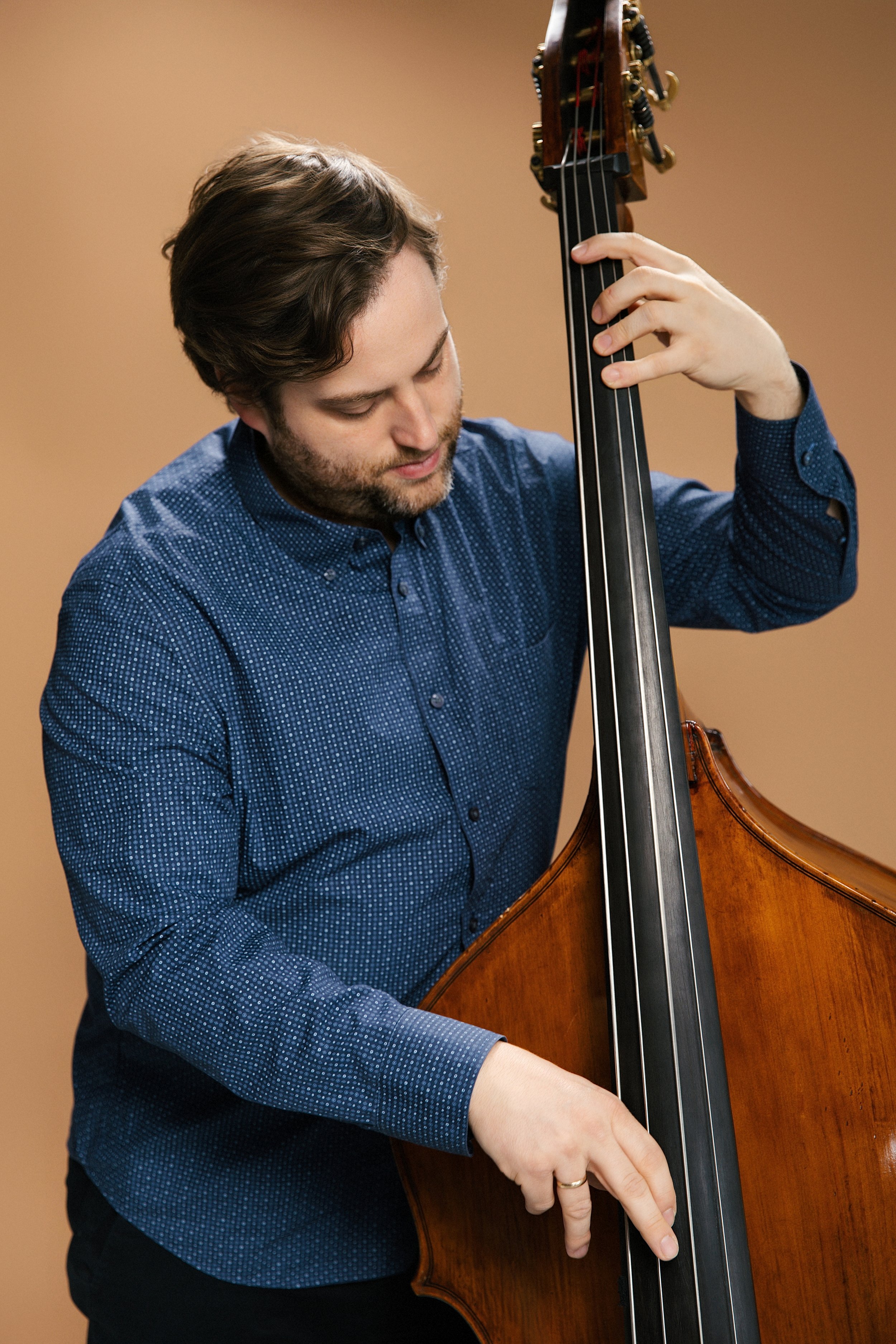 A man playing a double bass indoors against a plain brown wall.