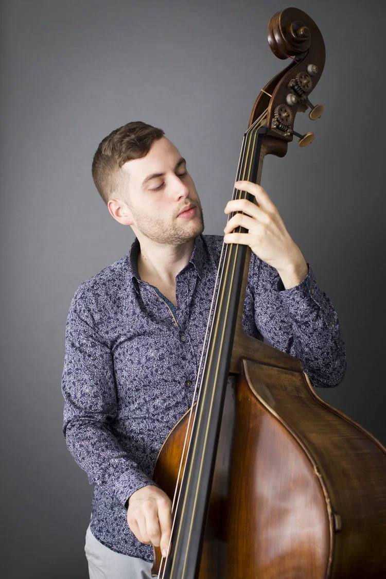 A man playing a double bass against a gray background.