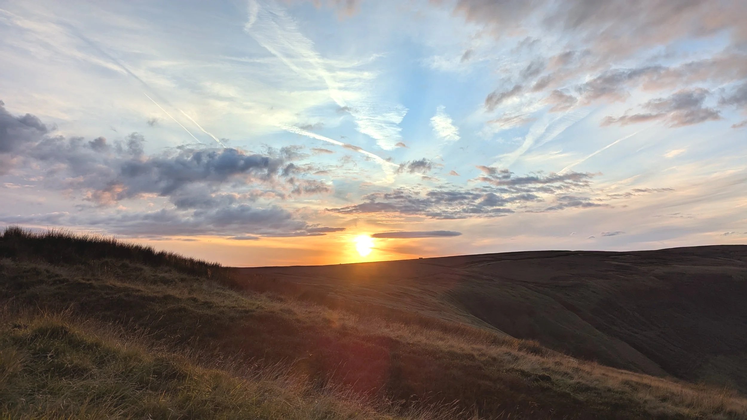 Scenic view of a sunset over rolling hills with a partly cloudy sky.