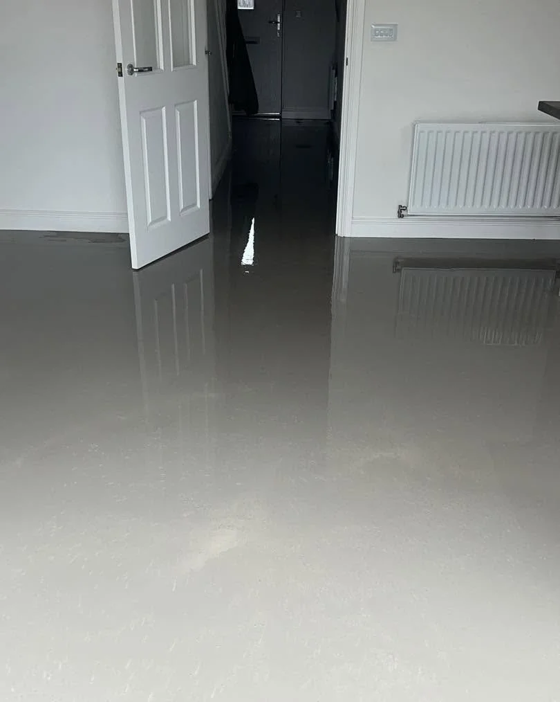 A clean screeded floor in a room with white walls and an open door leading to a darker hallway.