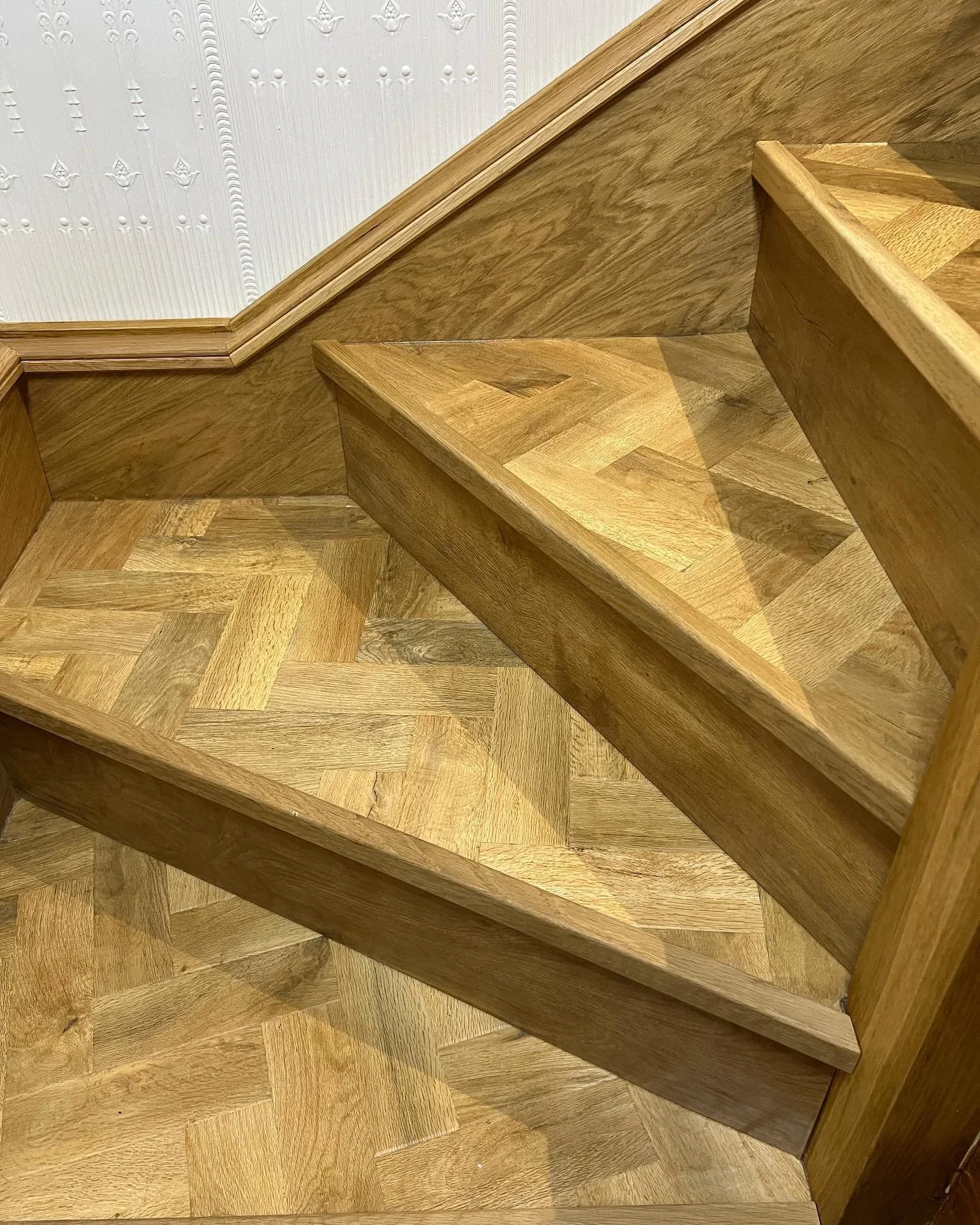 Close-up view of wooden stair steps and a wood-paneled wall with decorative white wallpaper.