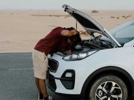A person checking the engine of a white SUV in a desert landscape.
