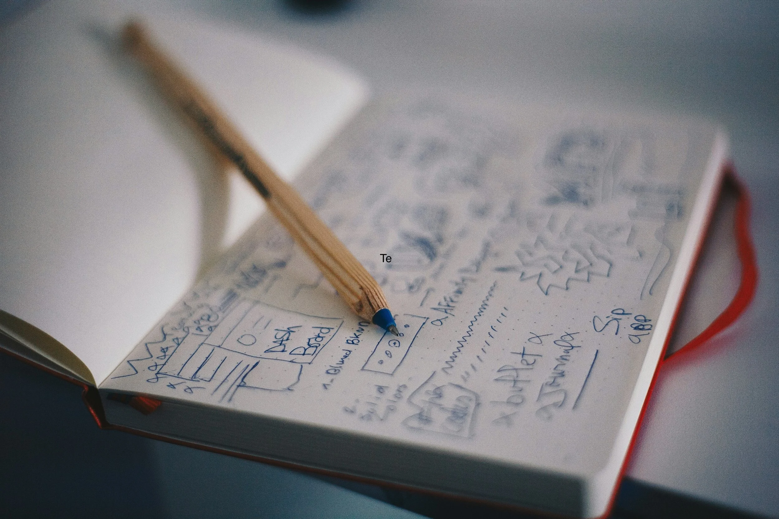 Open notebook with handwritten notes and sketches, a pen resting on the pages, and a white mug in the background.