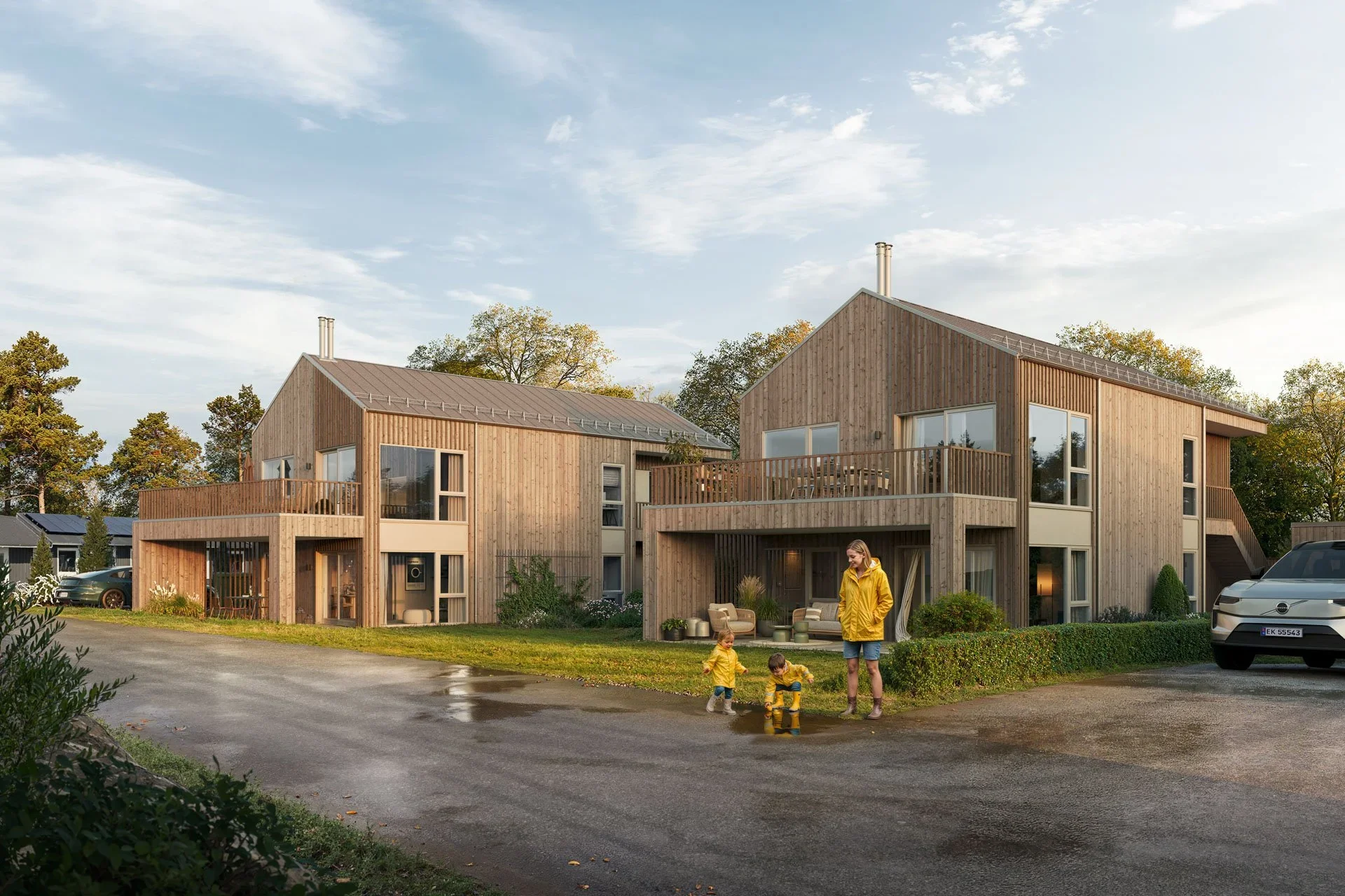 Moderne nybygg i Fredrikstad med store vinduer og balkonger, omgitt av grøntområder og trær, med mennesker som leker og nyter uteområdet.