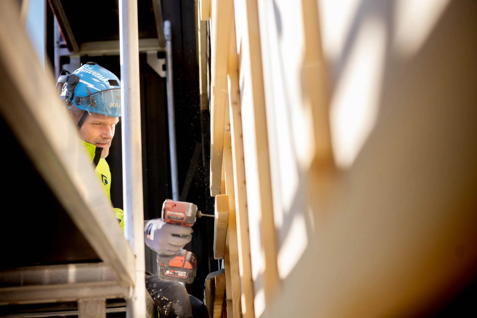 En byggmester med hjelm og refleksvest bruker en elektrisk drill under bygging eller reparasjon.