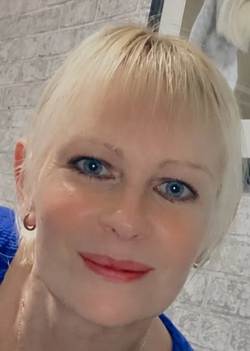 Close-up of a woman with short blonde hair and blue eyes, smiling.