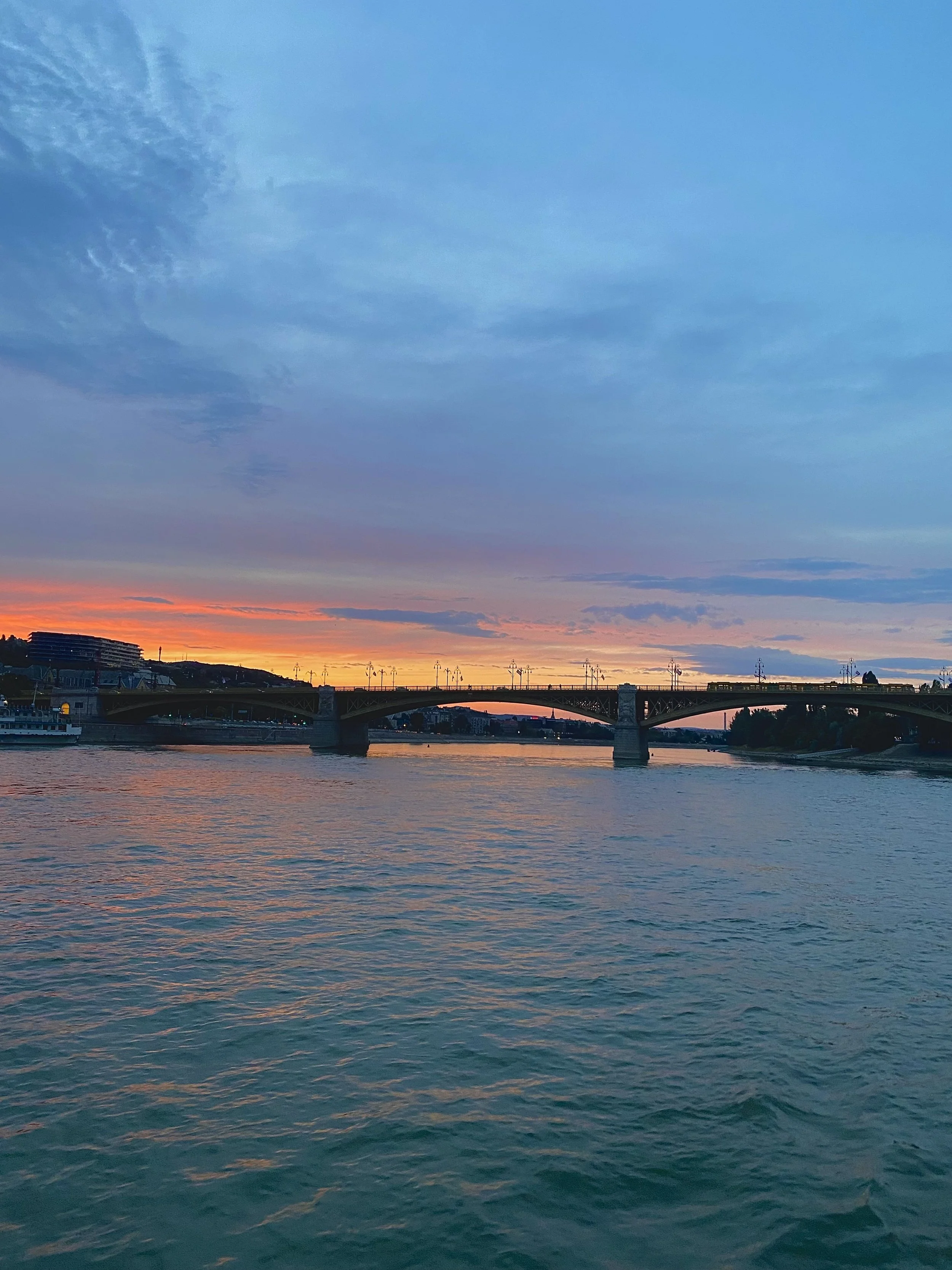 Sunset over a body of water with a bridge and cityscape in the background.