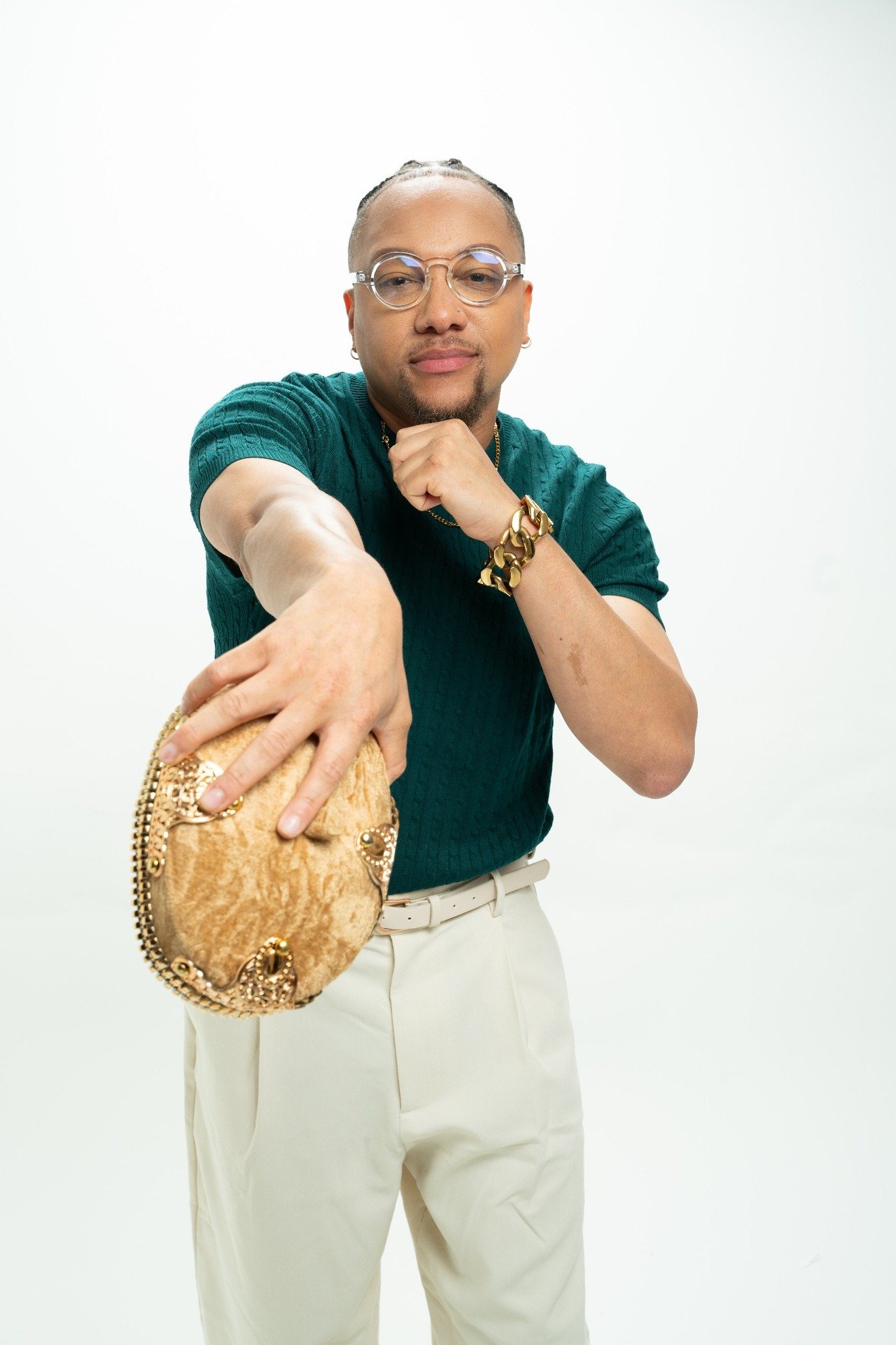 JoJo Crews with glasses and jewelry holding a small beige purse against a plain white background.