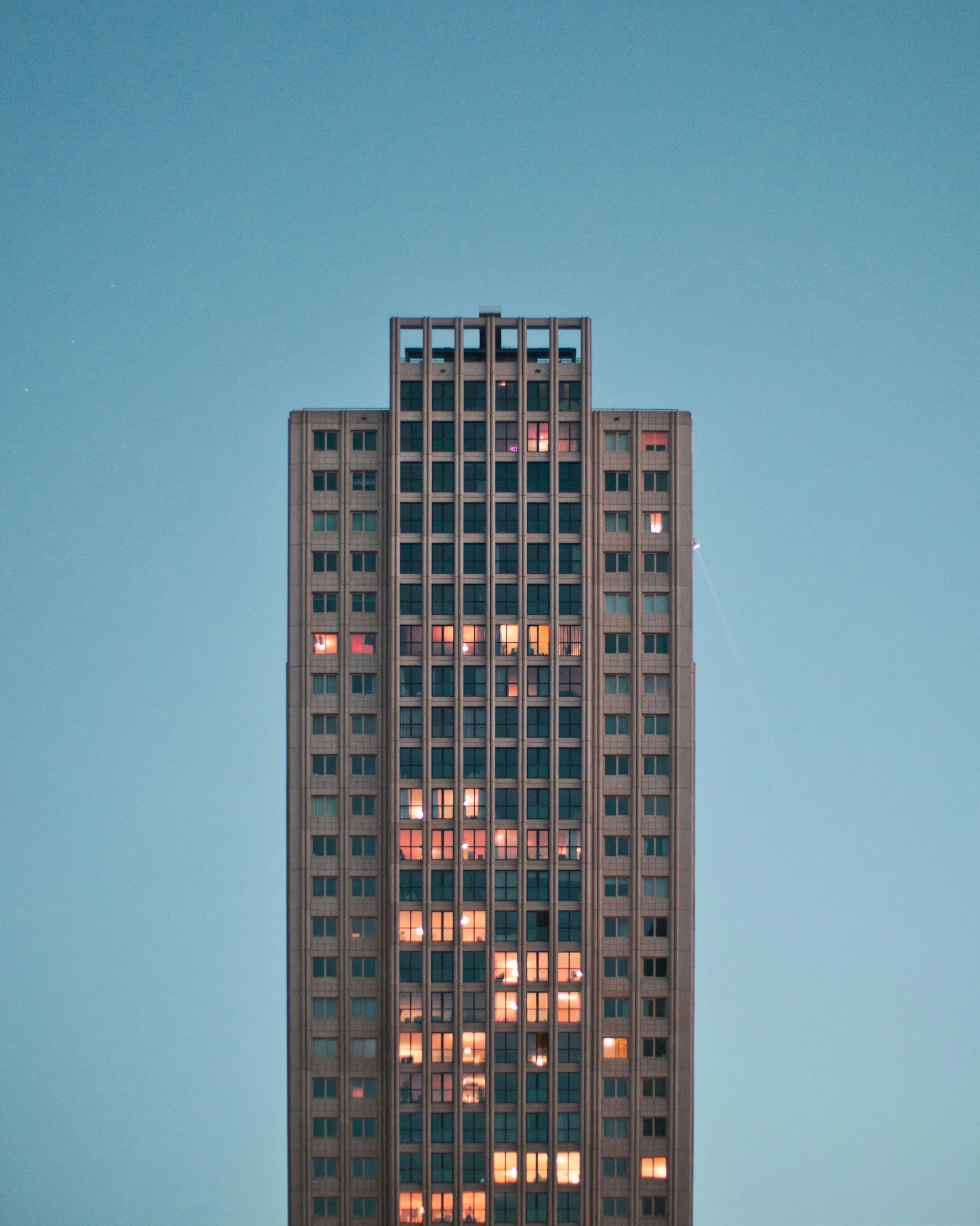 A tall building with several illuminated windows against a clear sky.