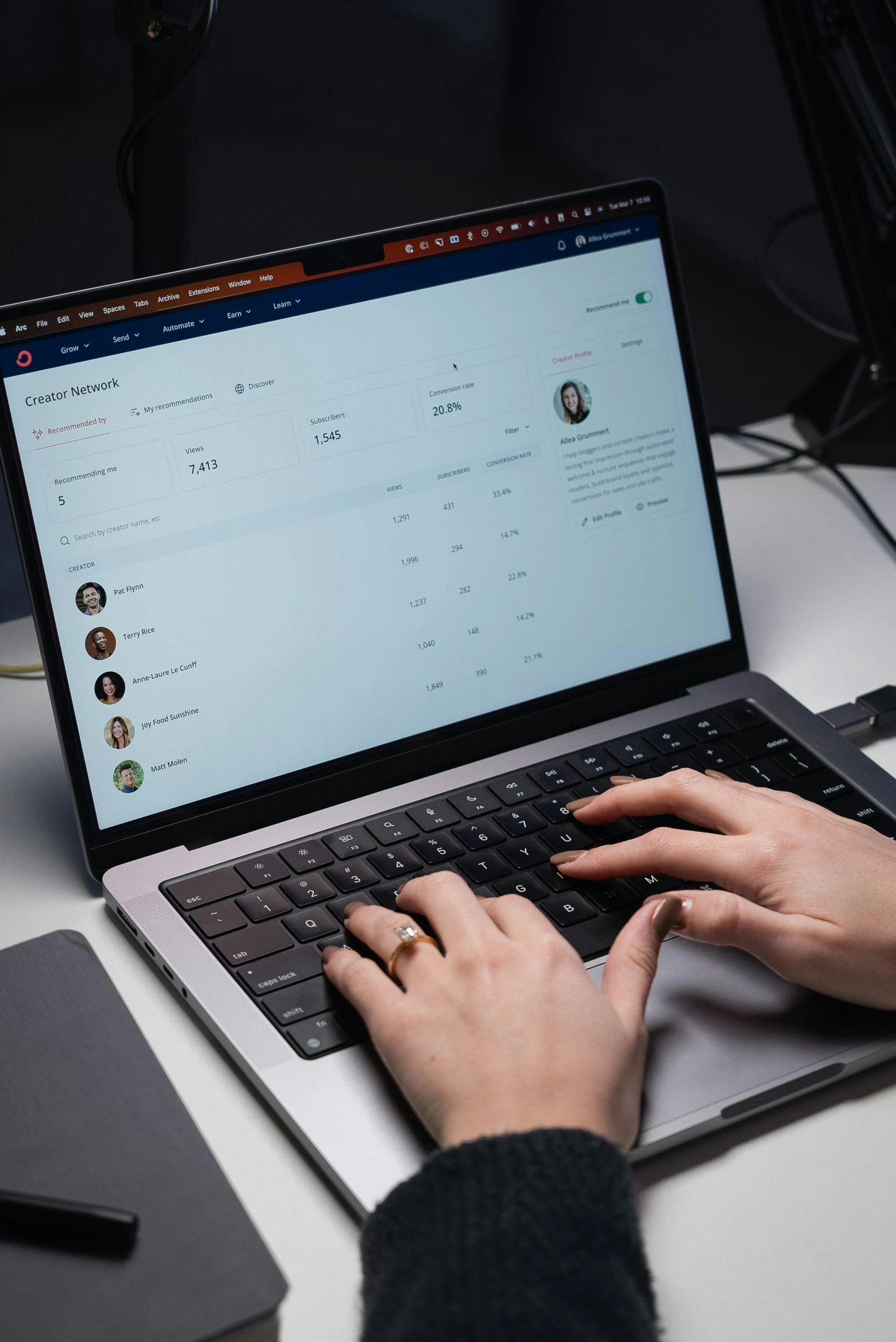 Laptop screen displaying Creator Network dashboard with statistics, profile picture, and user list, with person typing on keyboard.
