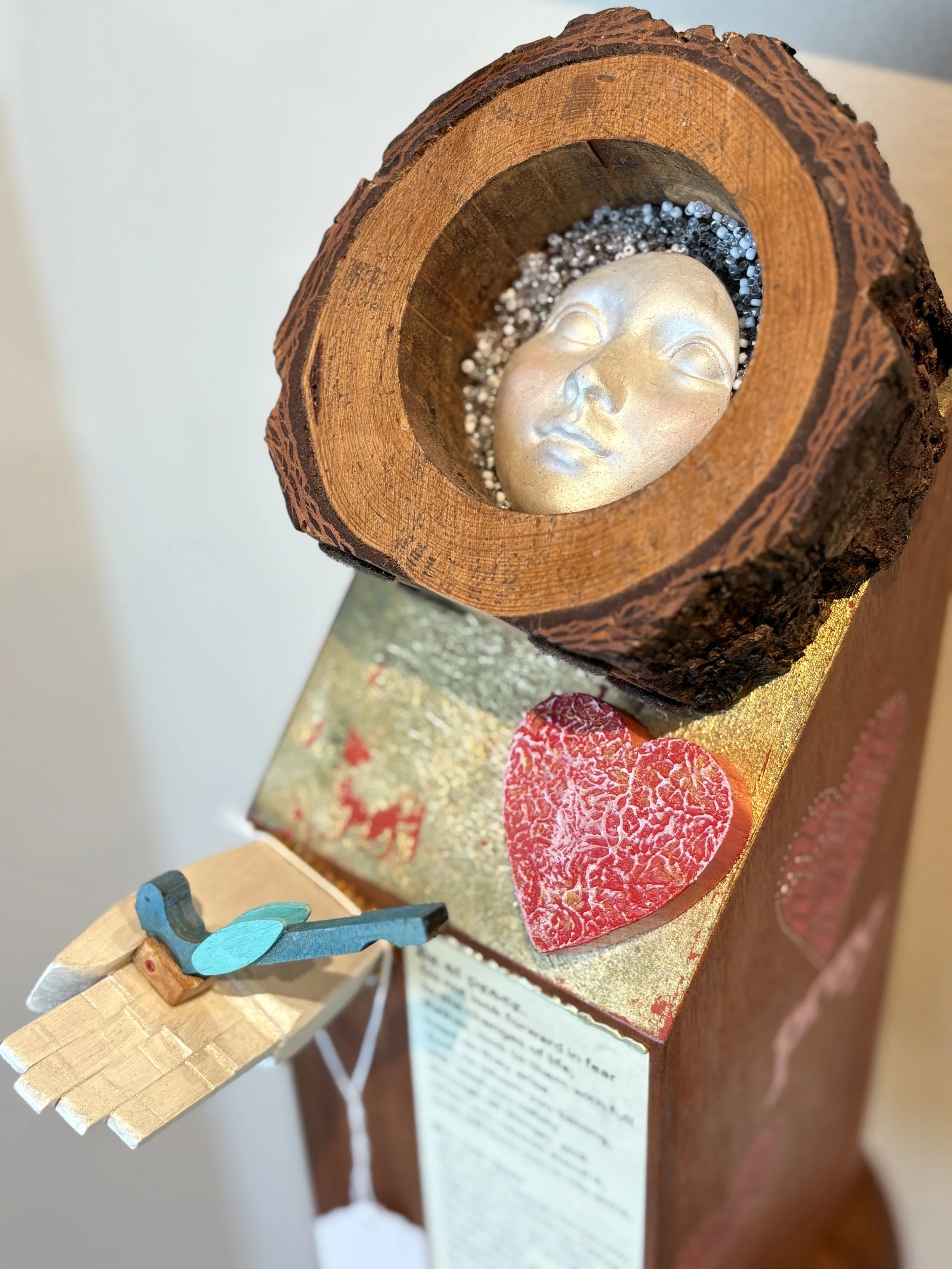 Wooden sculpture of a serene, closed-eyes human face surrounded by decorative elements, mounted on a wooden base.