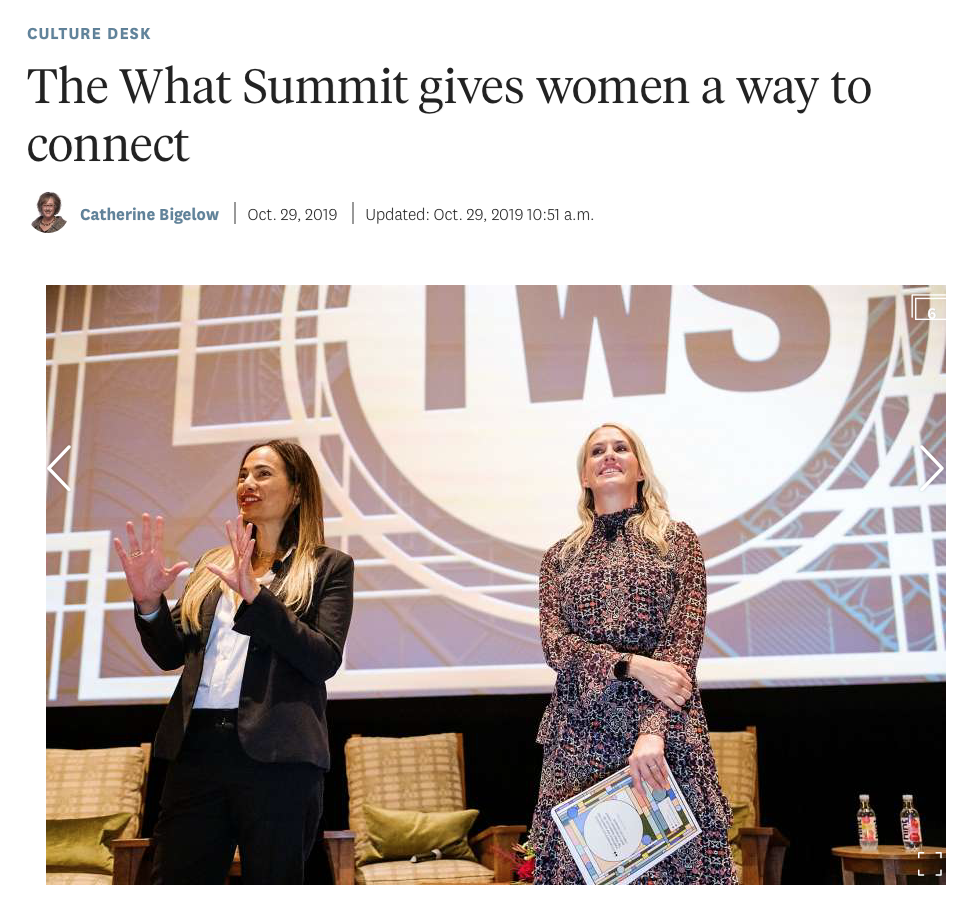 Two women are on stage at a conference or summit, with a large KWIS logo projected behind them. One woman is speaking and gesturing with her hands, while the other woman is holding a paper or certificate and smiling.