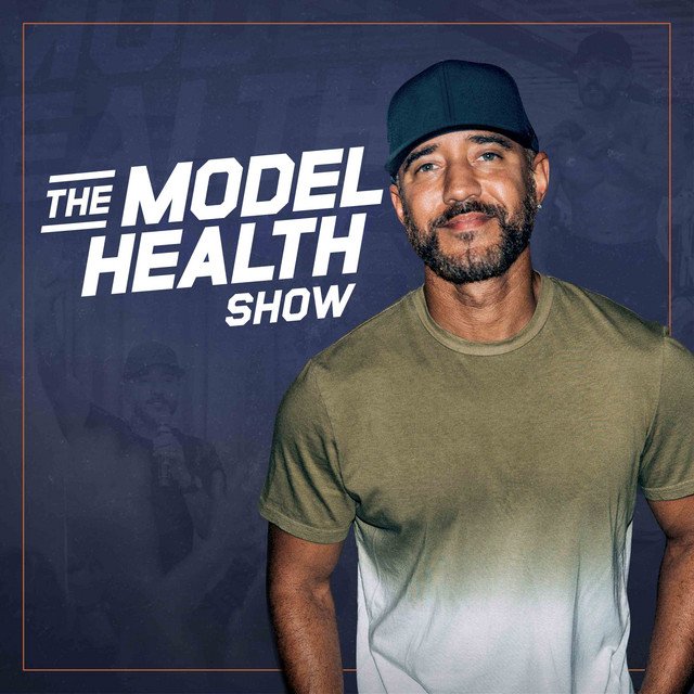 A man with a beard wearing a dark cap and olive-green t-shirt standing in front of a sign that reads 'The Model Health Show'.