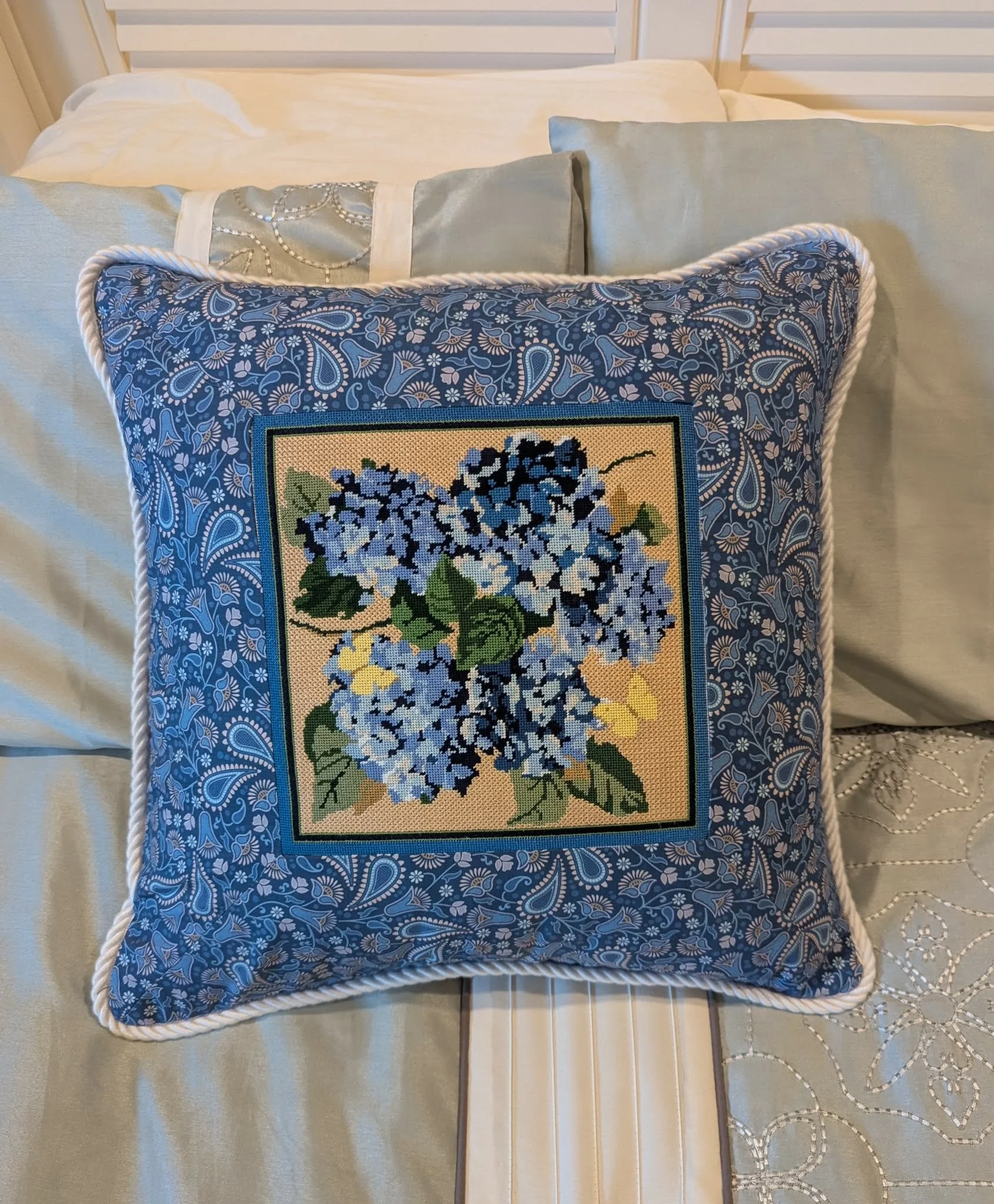 A  needlepoint pillow with a blue floral hydragea pattern.
