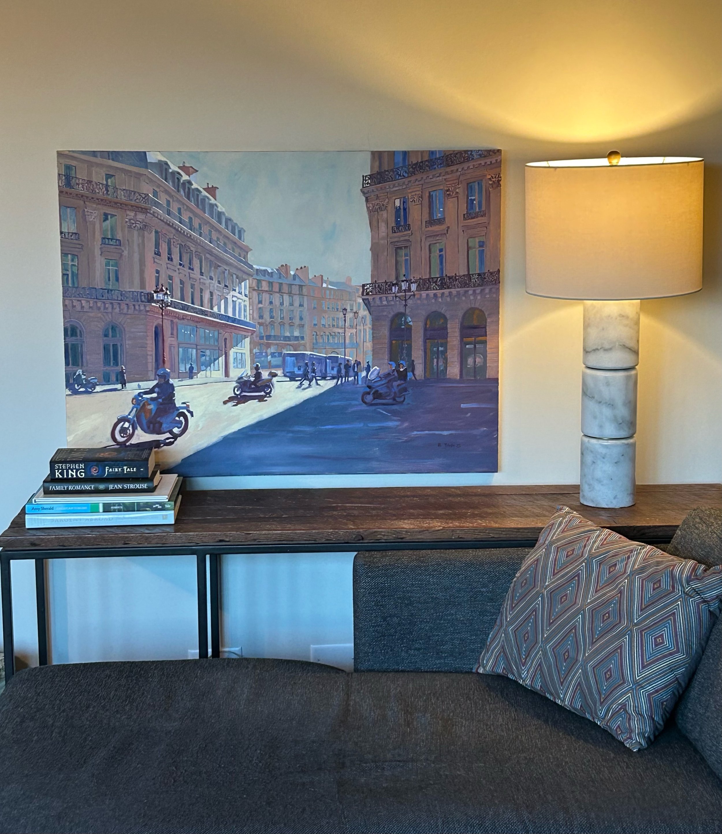 Painting of a busy Paris city street with tall buildings, motorcycles, and pedestrians, styled on a sofa table.