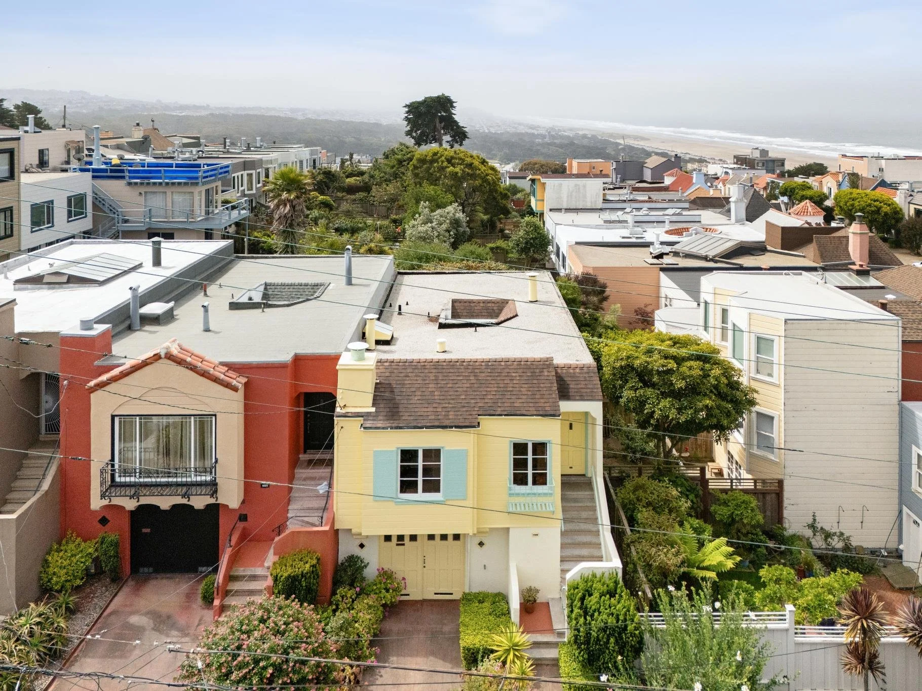 A cityscape view of colorful houses with gardens and trees, with a foggy ocean in the background and a clear sky above.