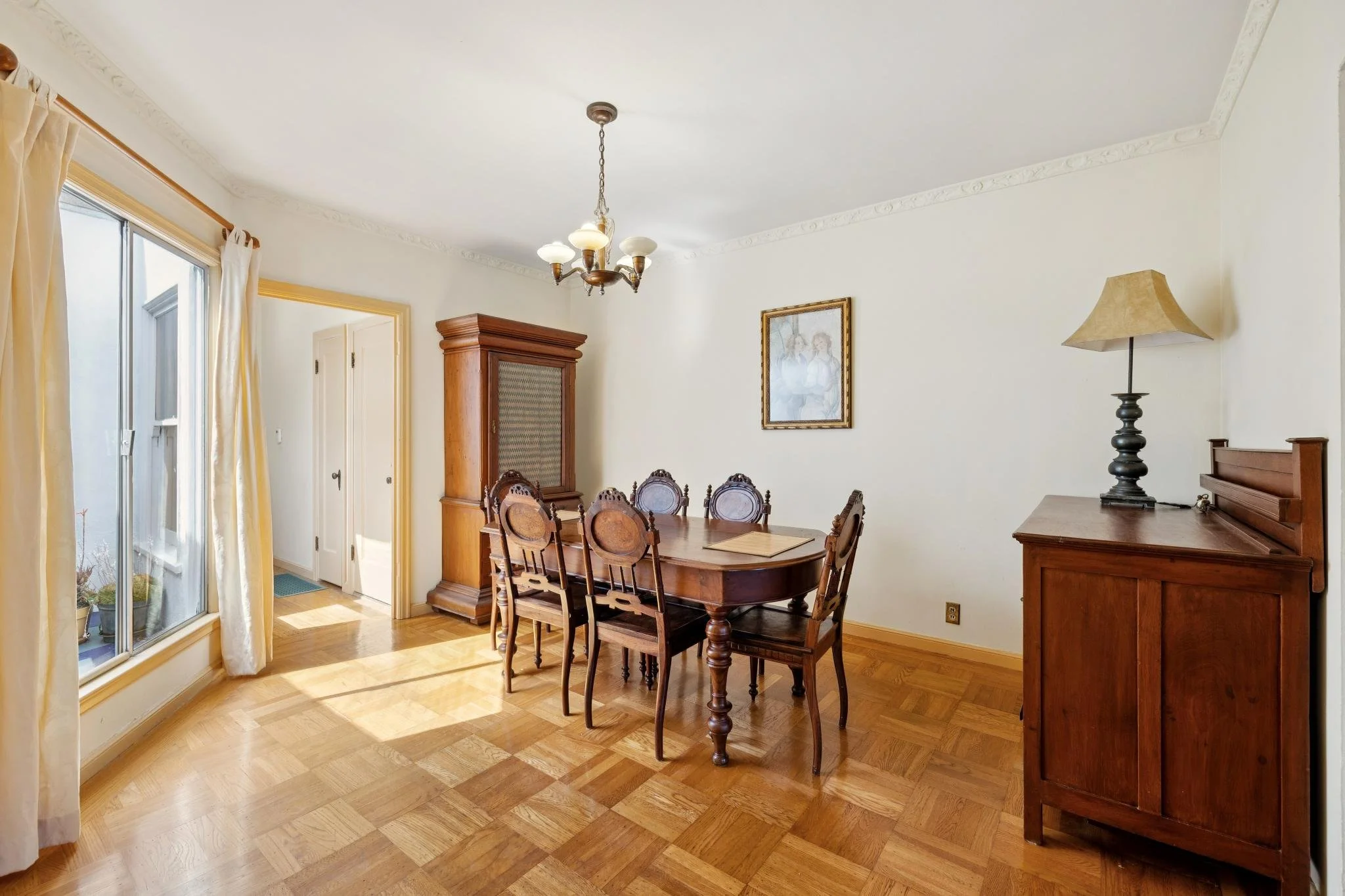 Dining room with a wooden table and chairs, a corner cabinet, a floor lamp, framed artwork on the wall, a sliding glass door with curtains, and hardwood flooring.