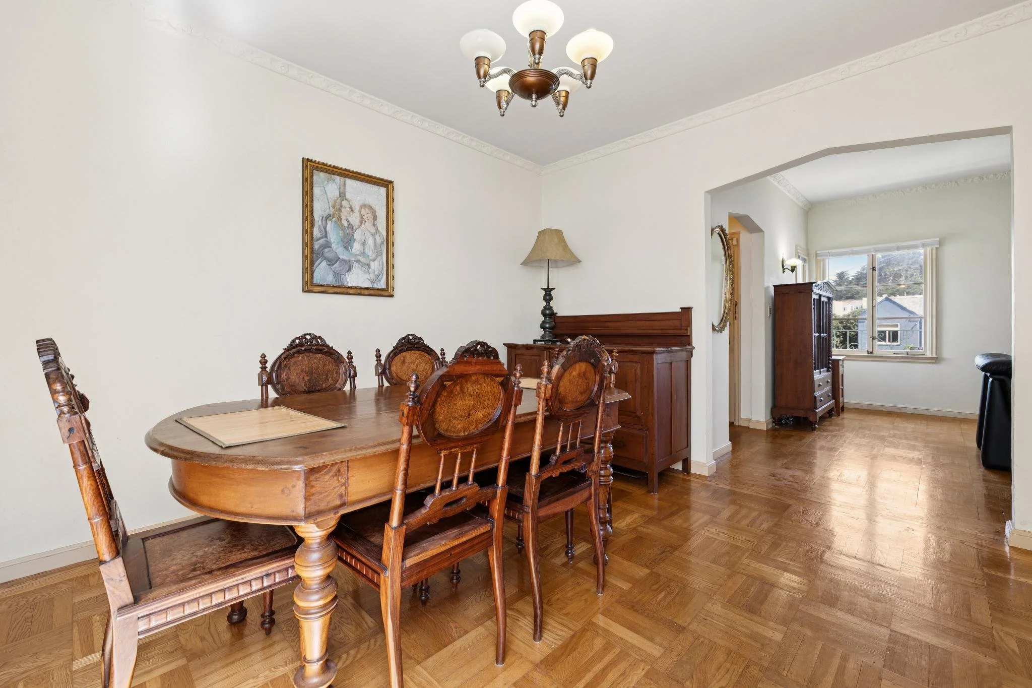 A dining room featuring a wooden table with matching chairs, a floor lamp, artwork on the wall, and a view of a window revealing neighboring houses.