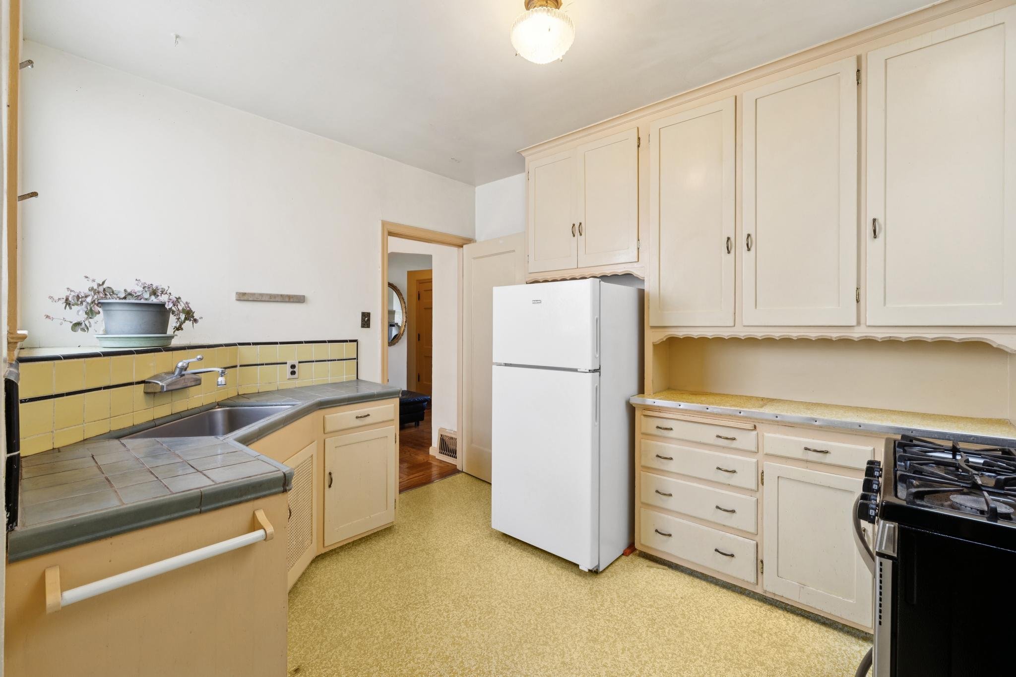 Kitchen with white cabinets, a white refrigerator, a stove, a counter with a yellow tiled backsplash, and a small potted plant on the counter.