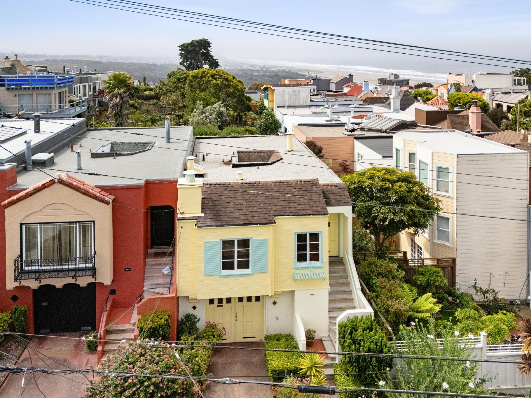 A view of colorful houses with trees and a distant ocean in the background, seen from a high vantage point.