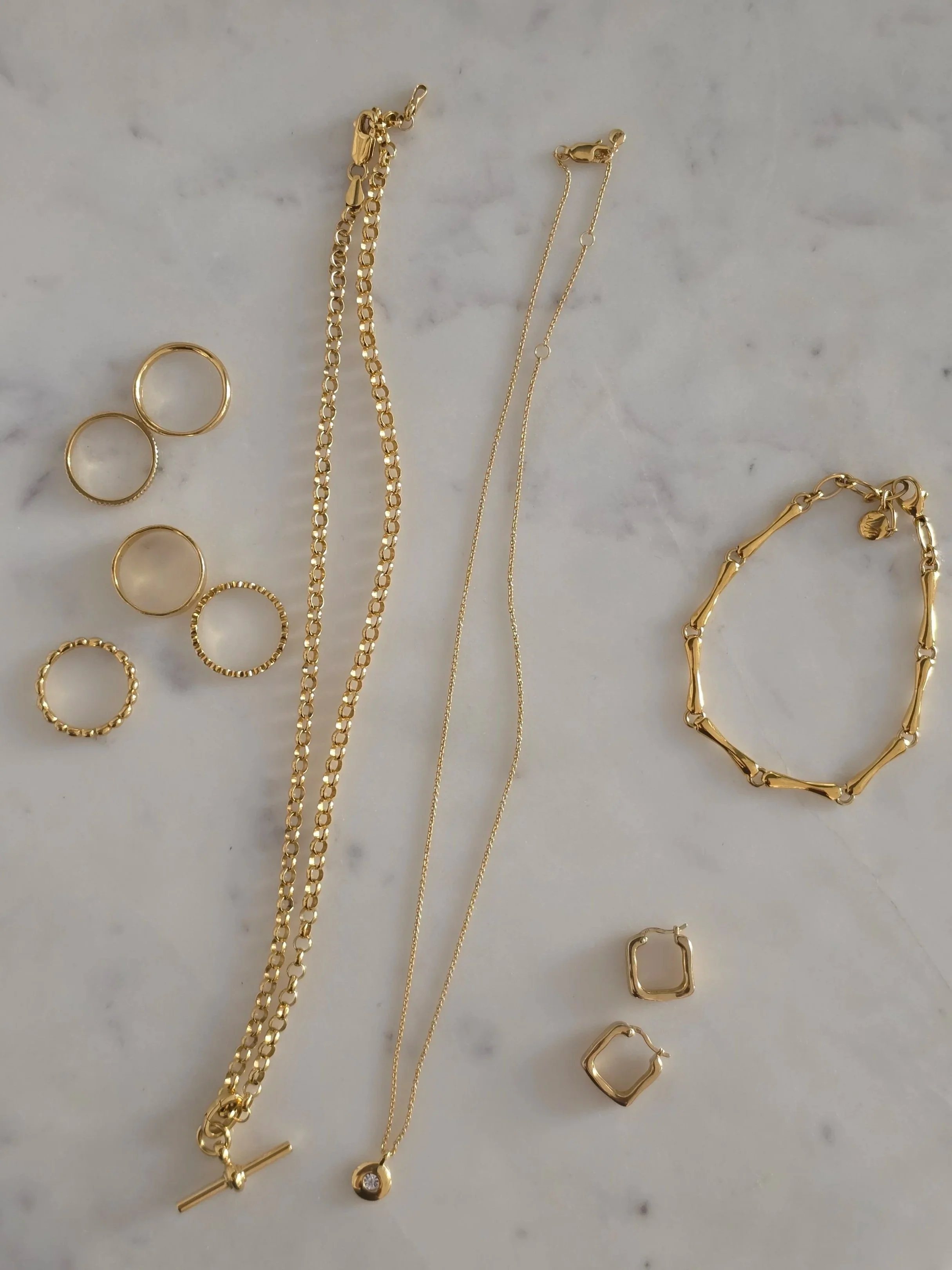 Collection of gold jewelry including rings, necklaces, and bracelets displayed on a marble surface.