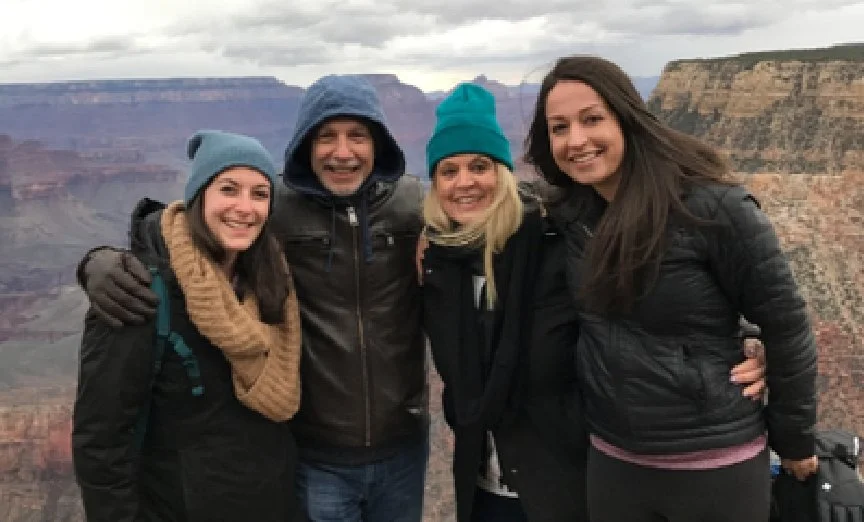 Four people smiling and posing together at the Grand Canyon, dressed warmly in jackets and beanies.