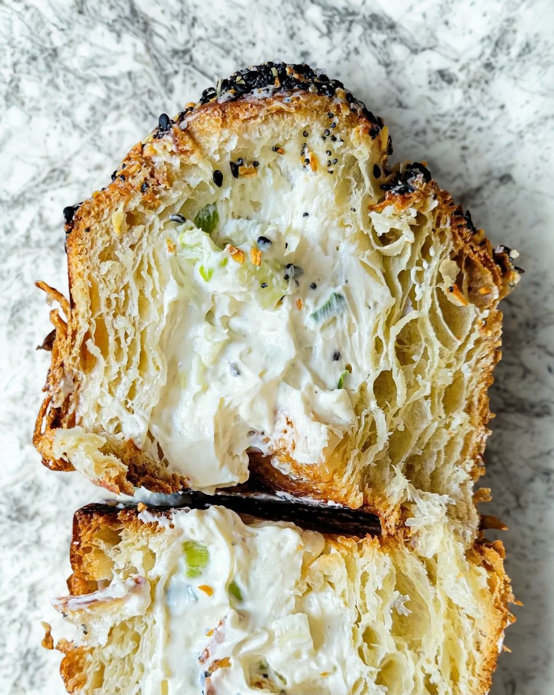 Close-up of a halved, muffin shaped croissant filled with scallion cream cheese, and topped with everything bagel seasoning in Myrtle Beach.