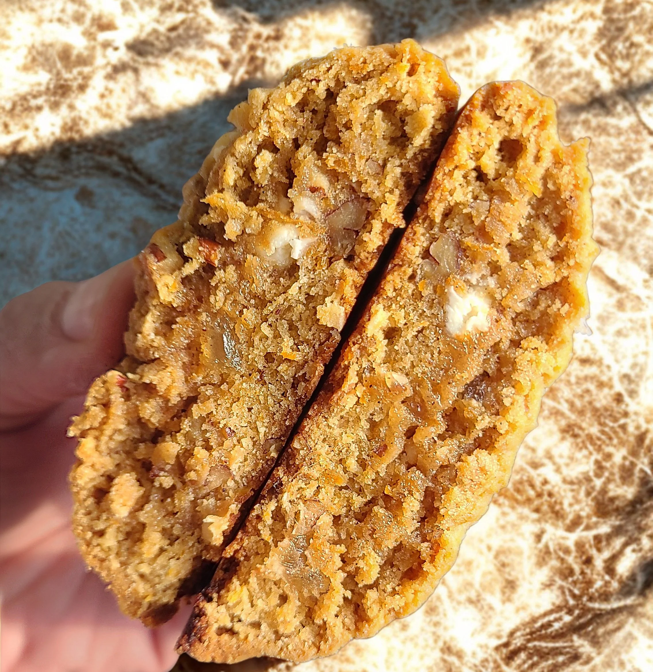 Close-up view of a yummy dessert cookie with a crumbly texture and visible crunchy nuts, being held by a hand, with more warm cookies blurred in the background in myrtle beach, south carolina at the soho shops in market common